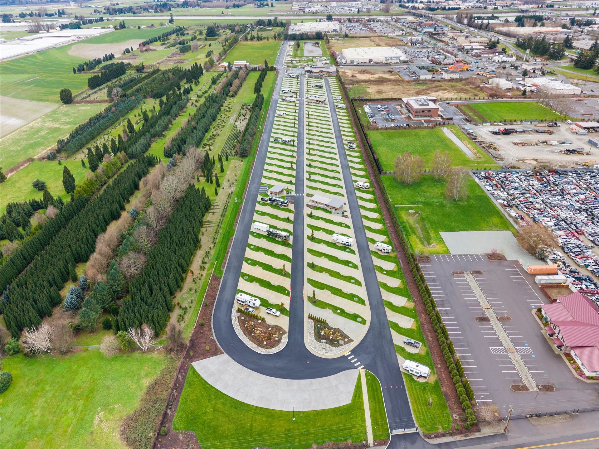 An aerial view of an RV park featuring paved lanes and angled parking spots, surrounded by fields and parked vehicles.