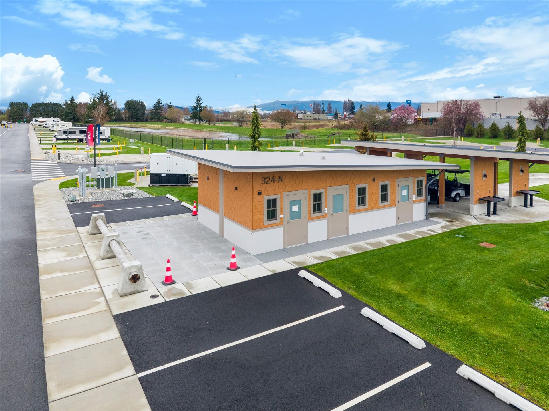 A modern, orange and white public restroom building sits next to a paved parking lot and a green grass area.