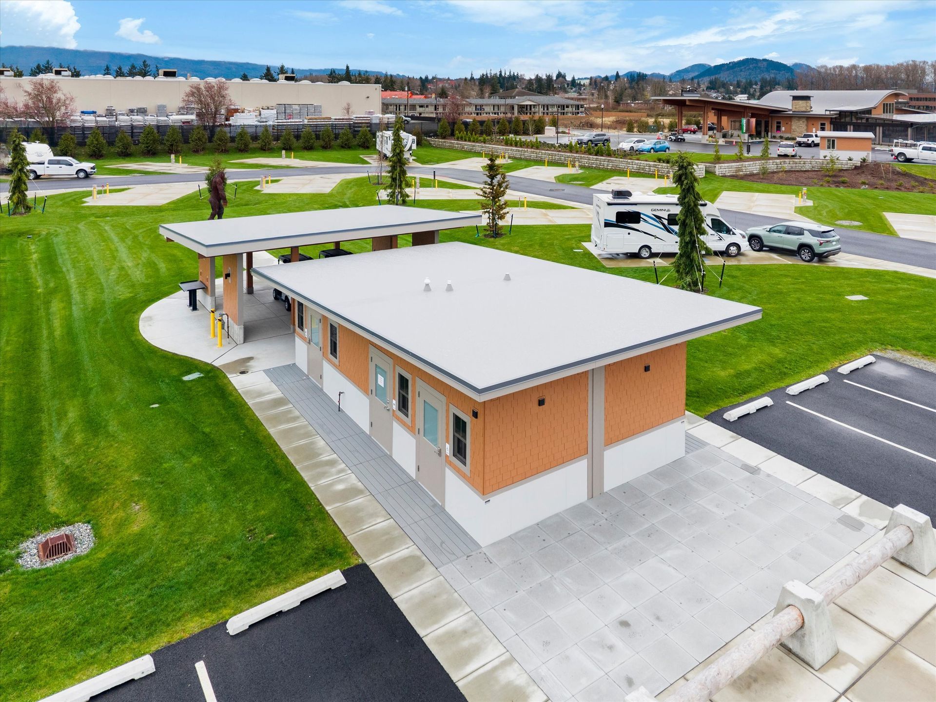 An aerial view of a tan and white public restroom building with a covered walkway in an RV park on a sunny day.