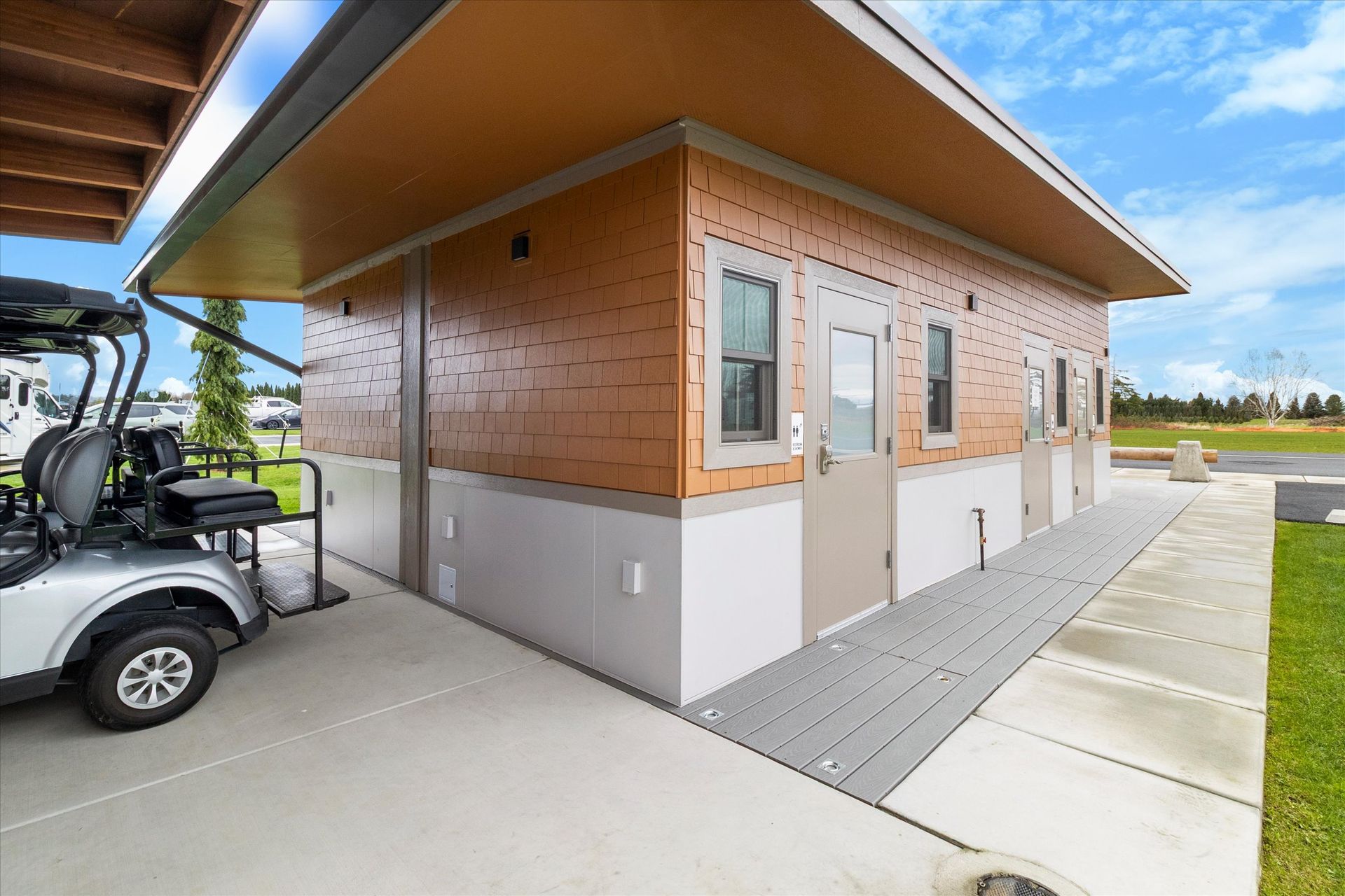 Modern tan building with multiple doors and a grey ramp, next to a parked golf cart on a concrete path.