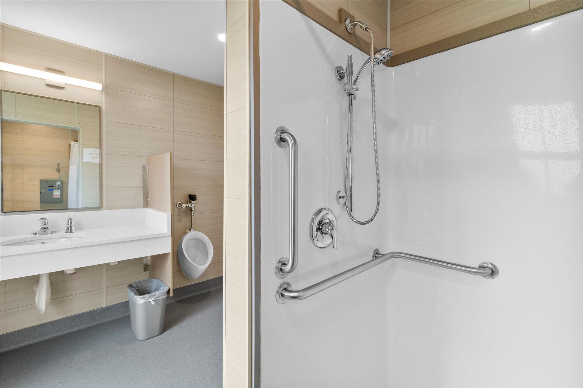 An accessible restroom featuring a walk-in shower with grab bars and a vanity area with a mirror and a urinal.
