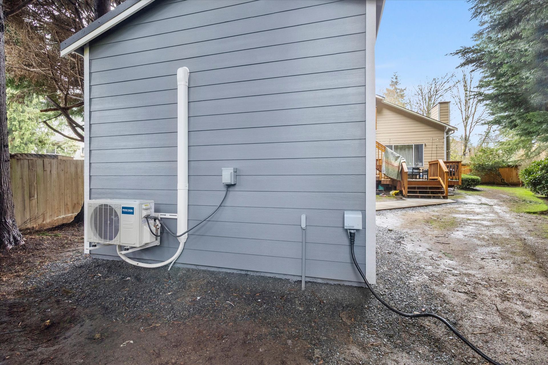 The exterior wall of a grey-sided structure features a mounted mini-split HVAC unit, conduit piping, and electrical boxes.