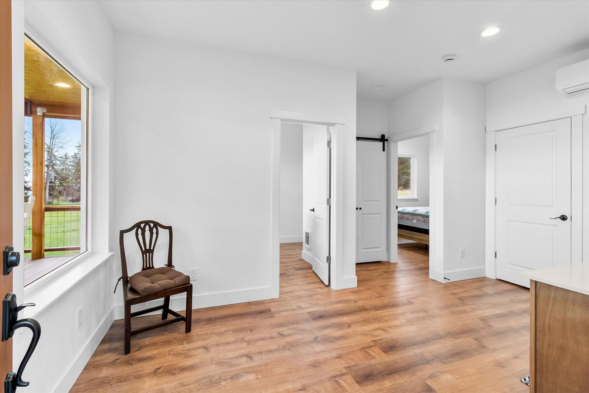 A bright, empty room with wood floors, a wooden chair by a window, white walls, and multiple white doors.