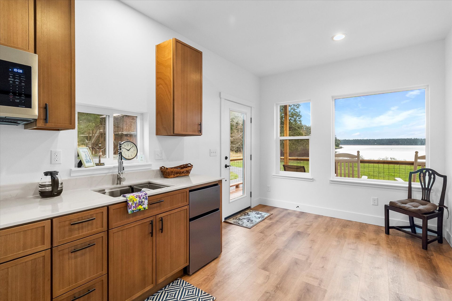 A bright kitchen with wood cabinets, white countertops, stainless appliances, and large windows overlooking a waterfront.
