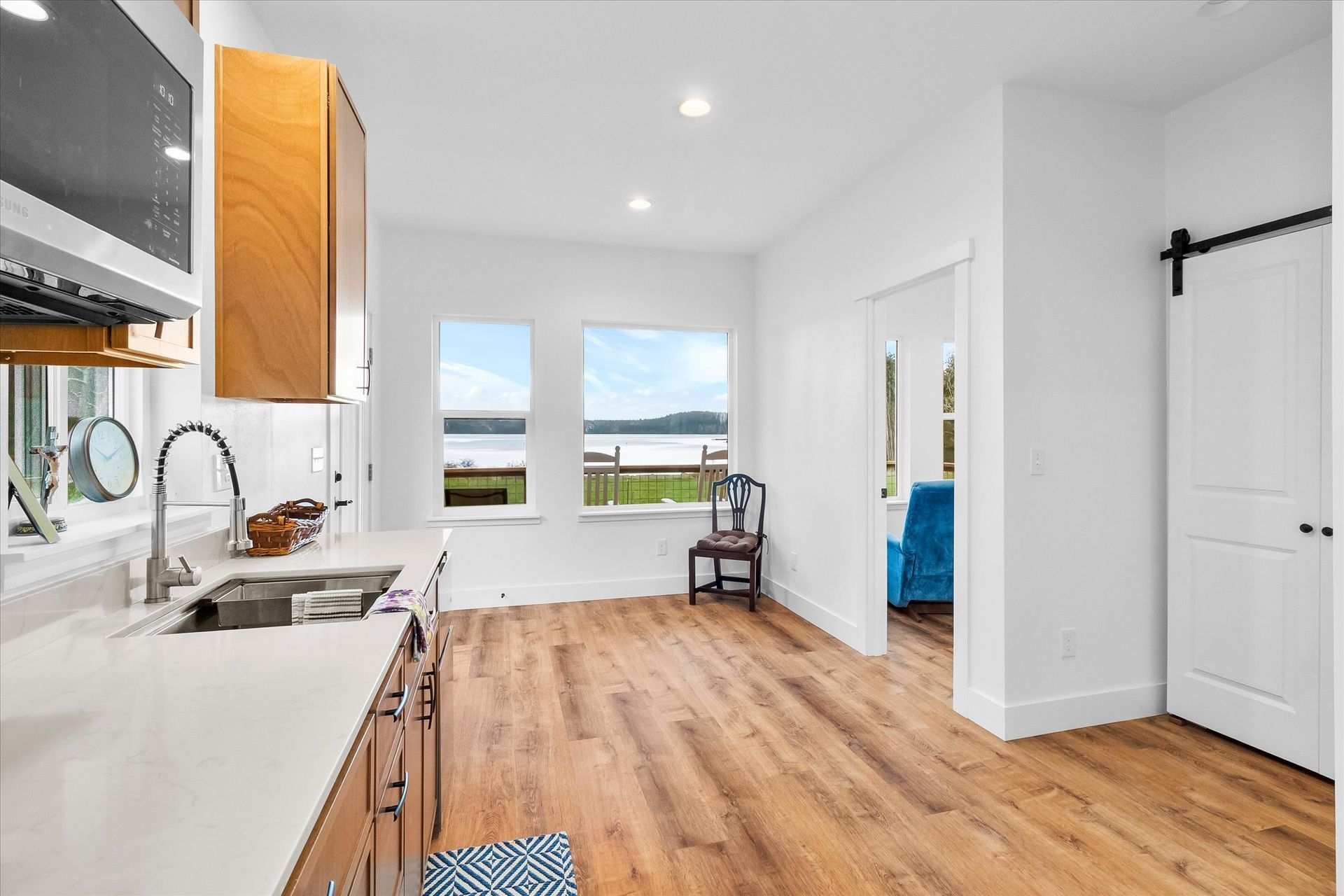 A modern kitchen with light wood floors, white countertops, wooden cabinets, and a scenic view of a body of water.