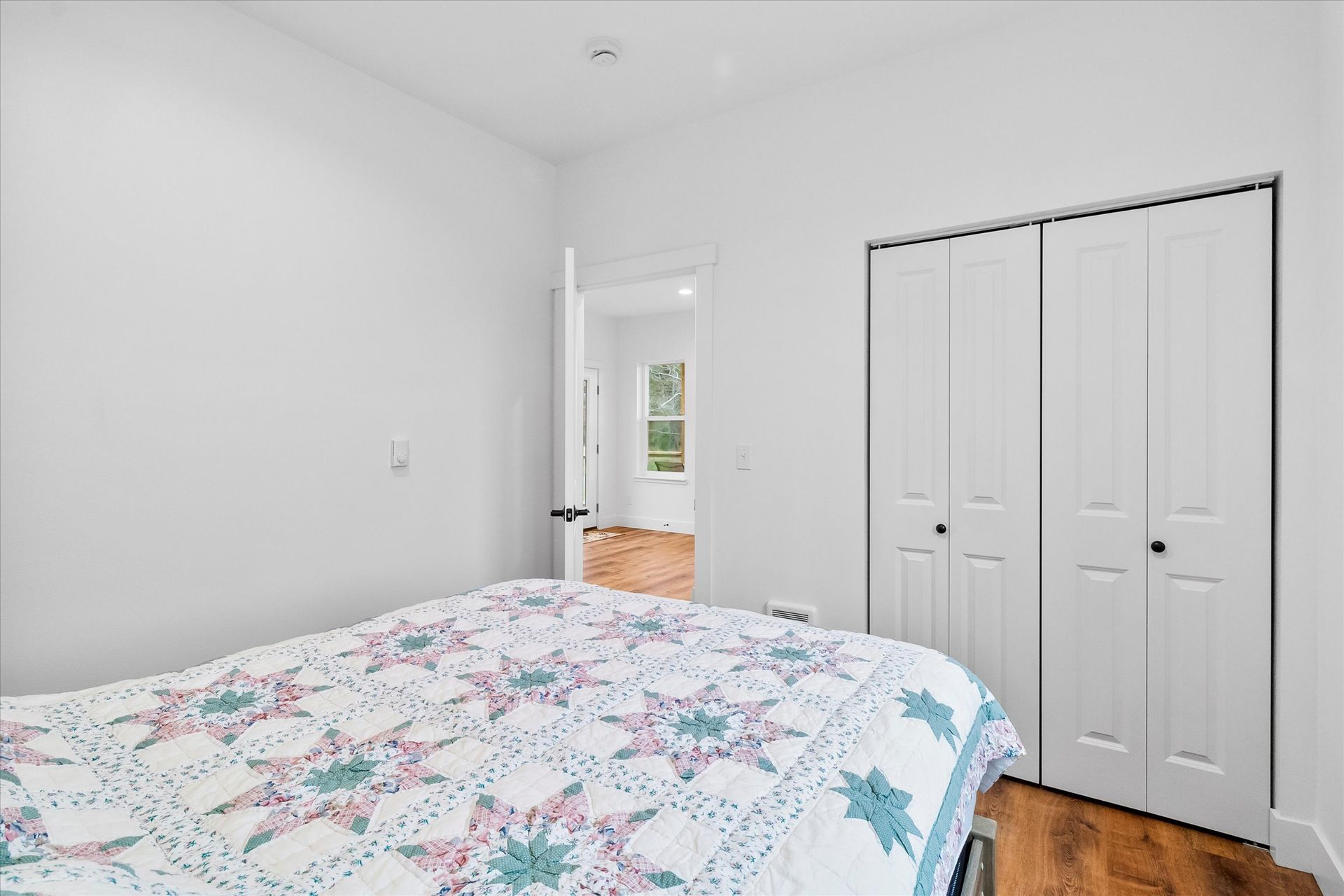 A bedroom with a bed featuring a star-patterned quilt, a closed white bifold closet, and an open door to a hallway.