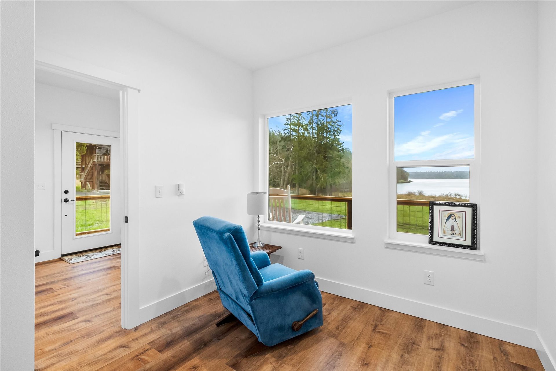 A blue recliner sits in a bright, modern room with two large windows overlooking a waterfront view.