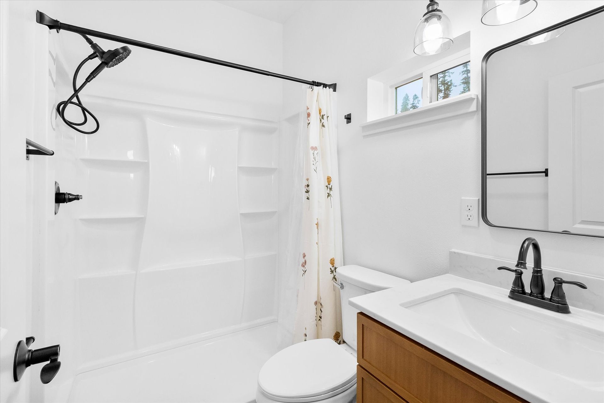 A modern bathroom featuring a white shower-tub combo, a vanity with a white countertop, and a mirror against white walls.