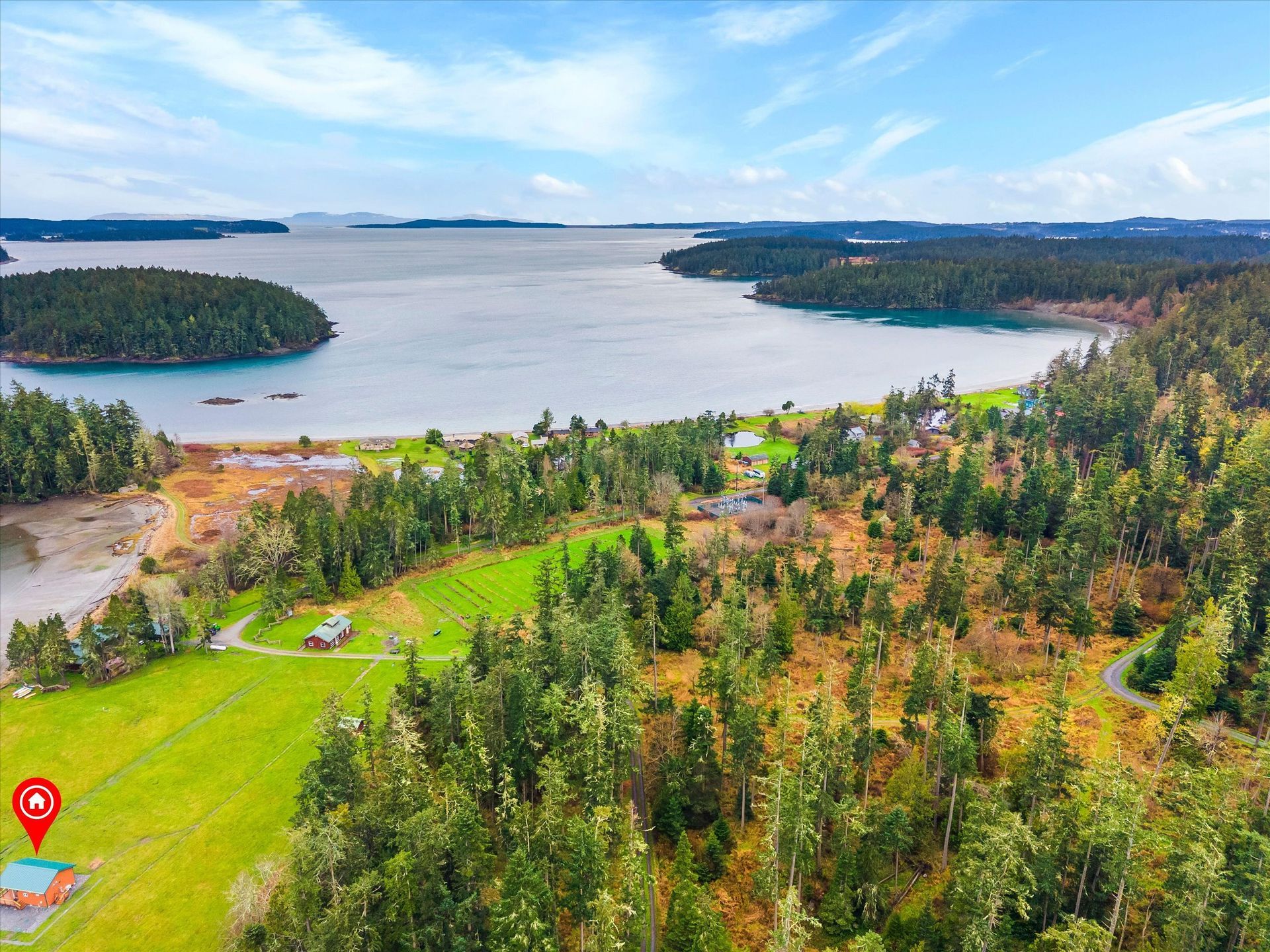 Aerial view of a coastal property with a grassy field, wooded areas, and a small pool by the water.
