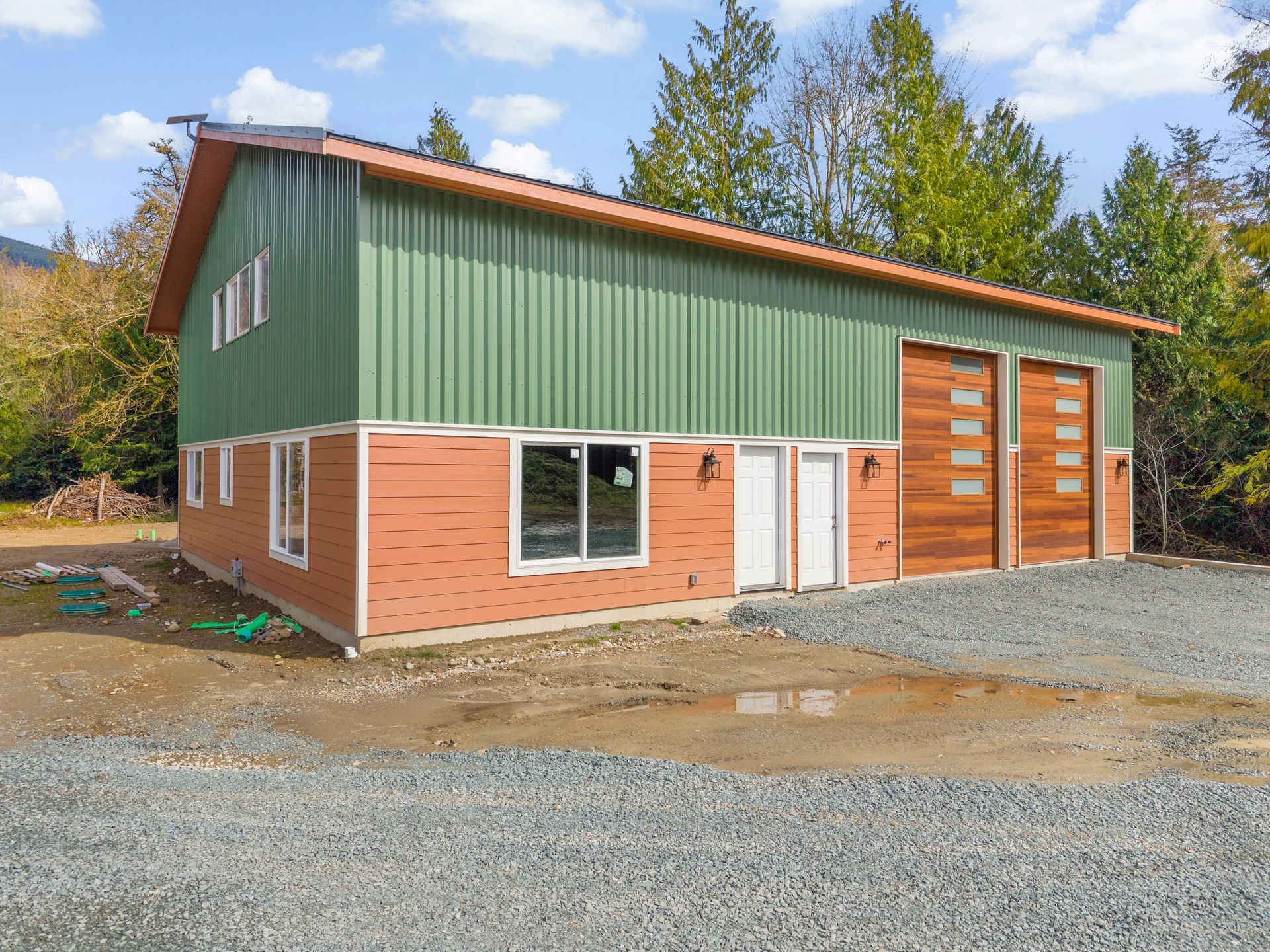 A two-story metal barn with green upper siding and orange horizontal lower siding, featuring garage and regular doors.