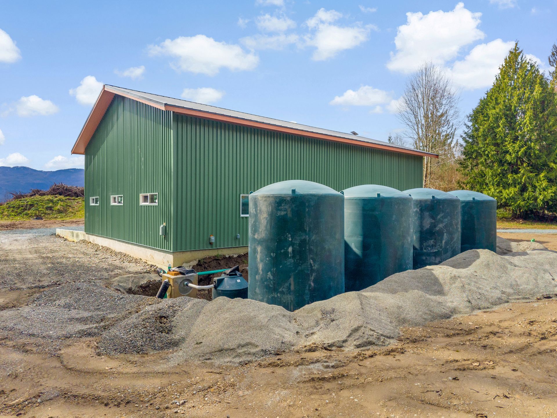 Green metal building with four large cylindrical green water tanks sitting on gravel in a rural landscape.