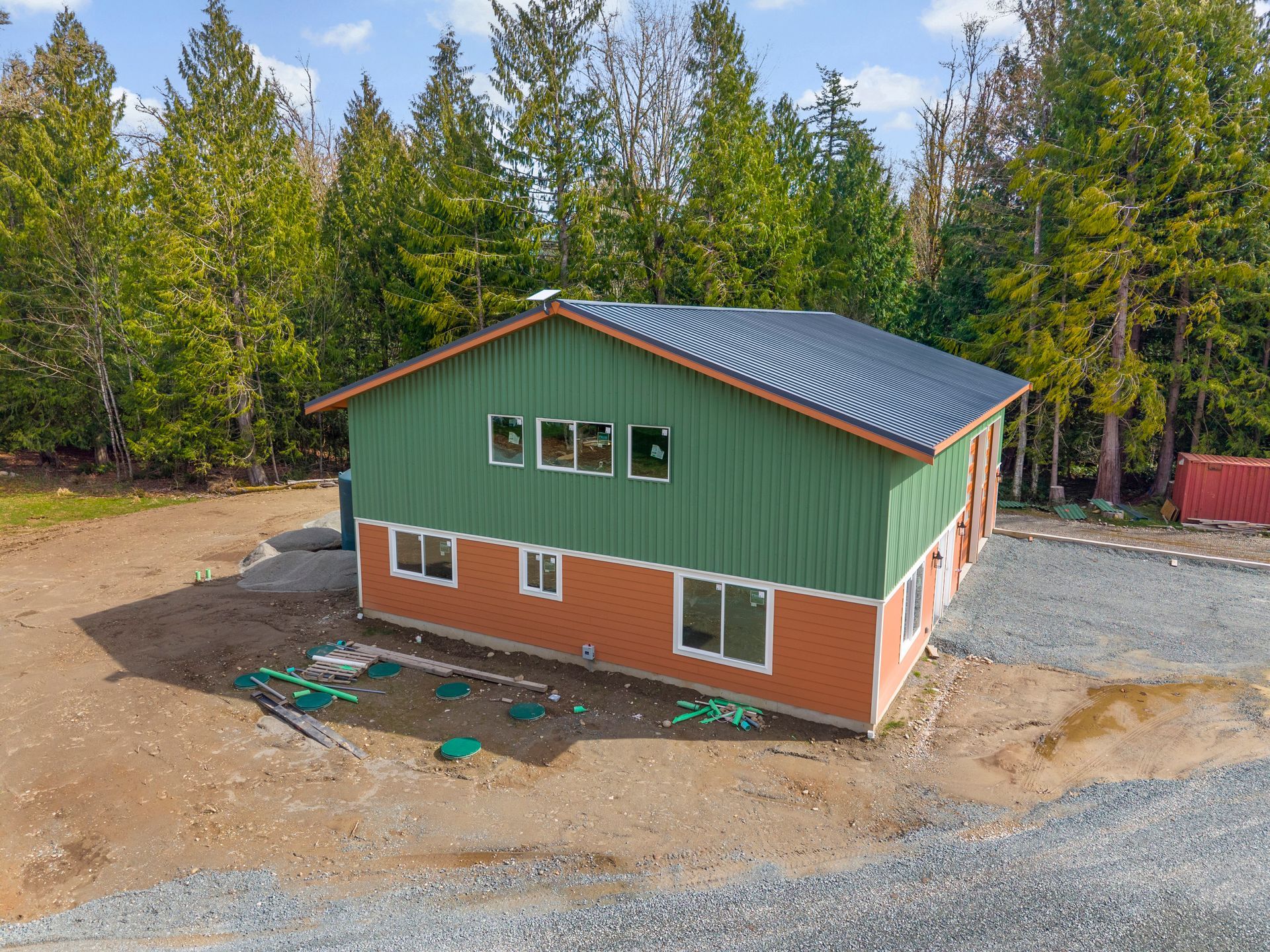 An elevated view of a two-story house with green upper siding and an orange brick-patterned lower exterior by a forest.