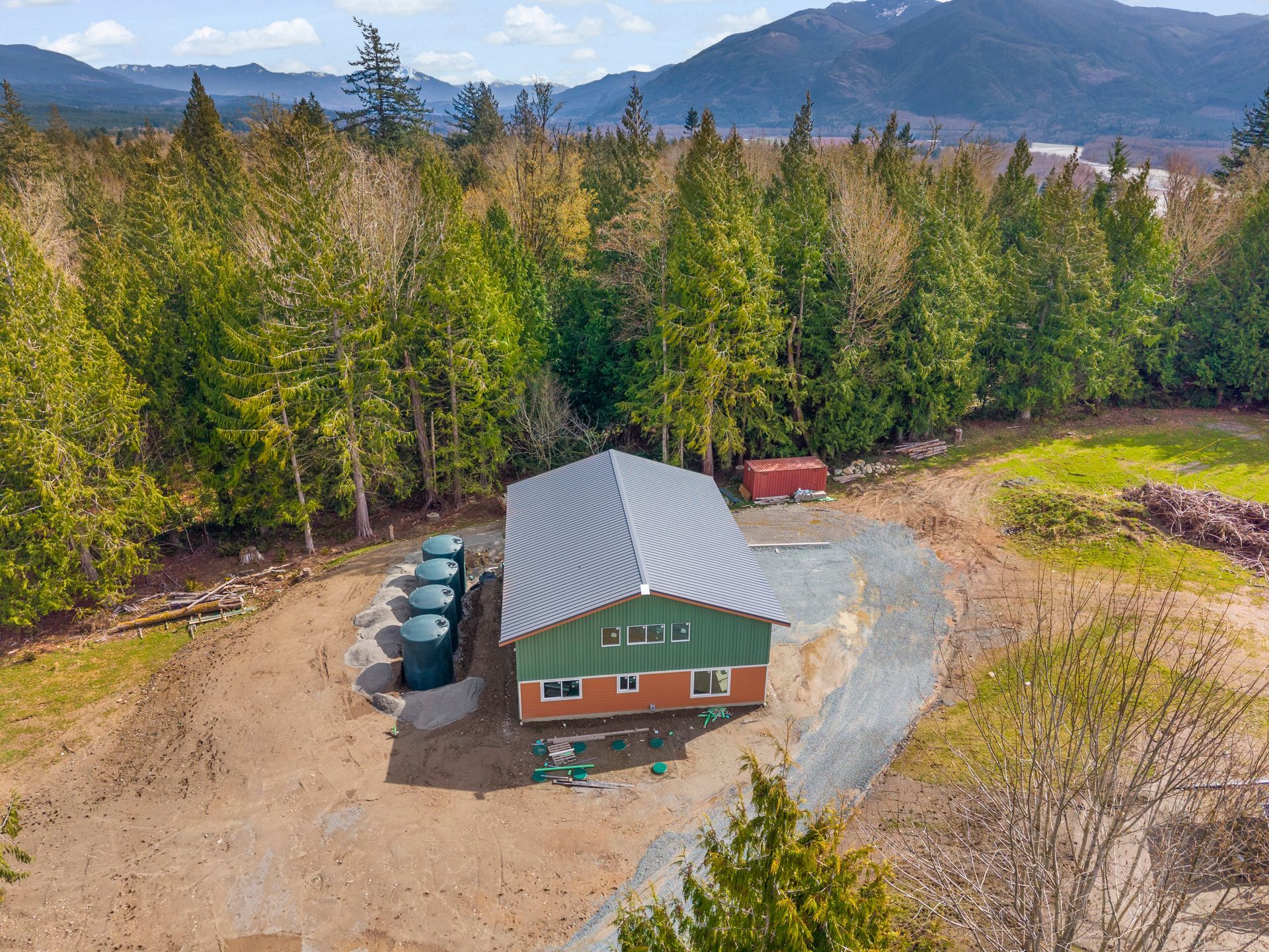 An aerial view of a green and brick house with four water tanks beside a forest and mountain landscape.