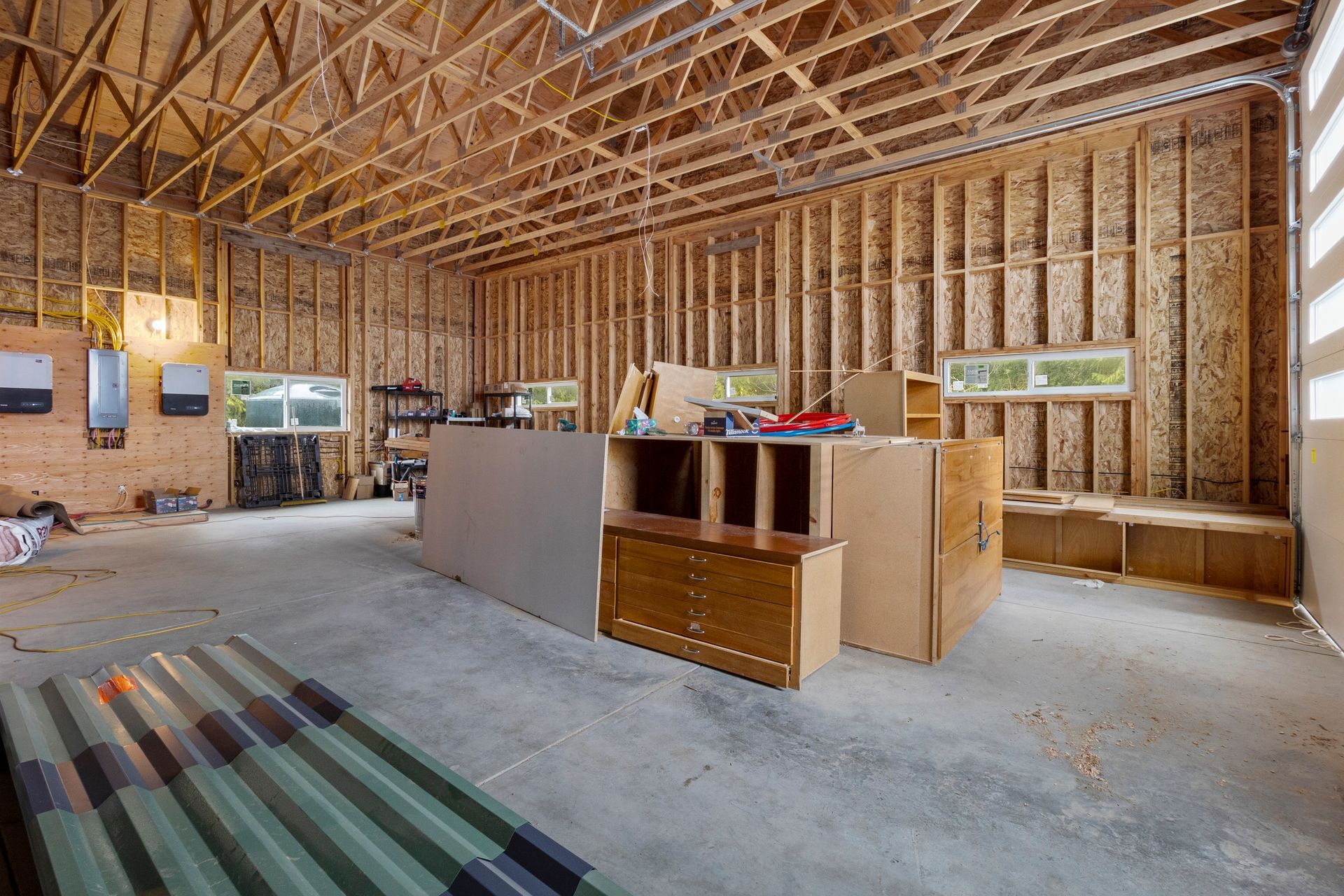 An unfinished garage with wooden wall framing and exposed rafters, featuring scattered construction supplies and tools.