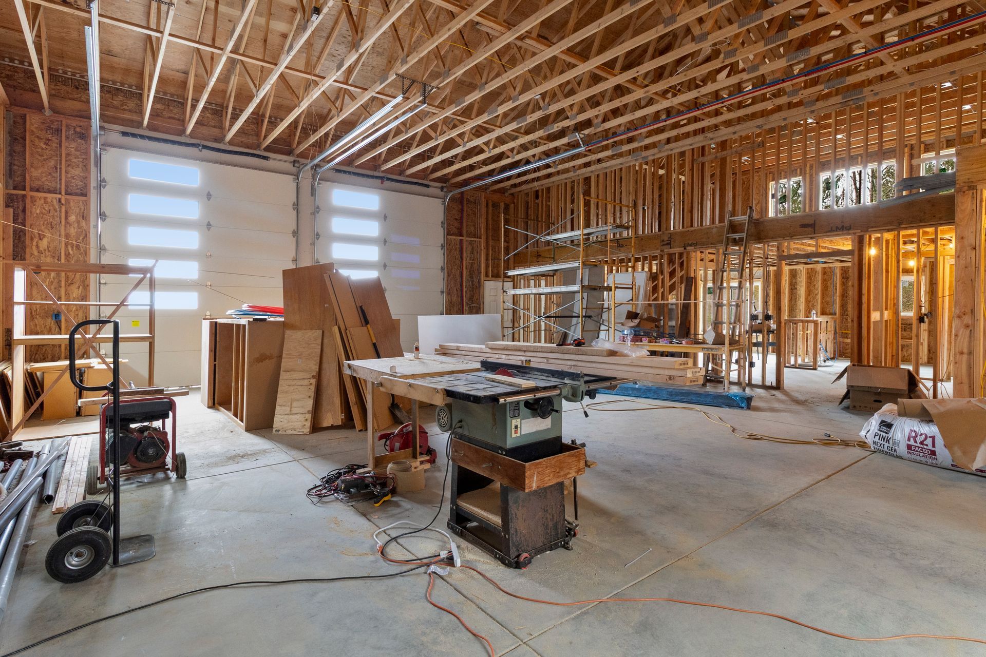 Interior of a building under construction, featuring exposed wooden framing, concrete floors, and a workbench with tools.