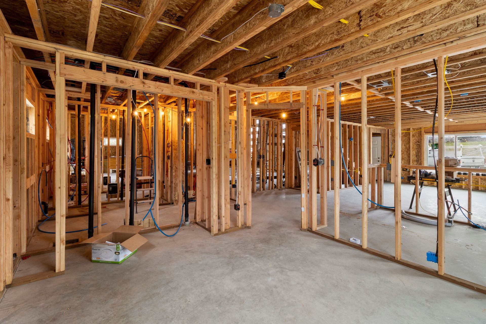 Interior view of a residential construction site featuring wooden framing, exposed ceiling joists, and a concrete floor.