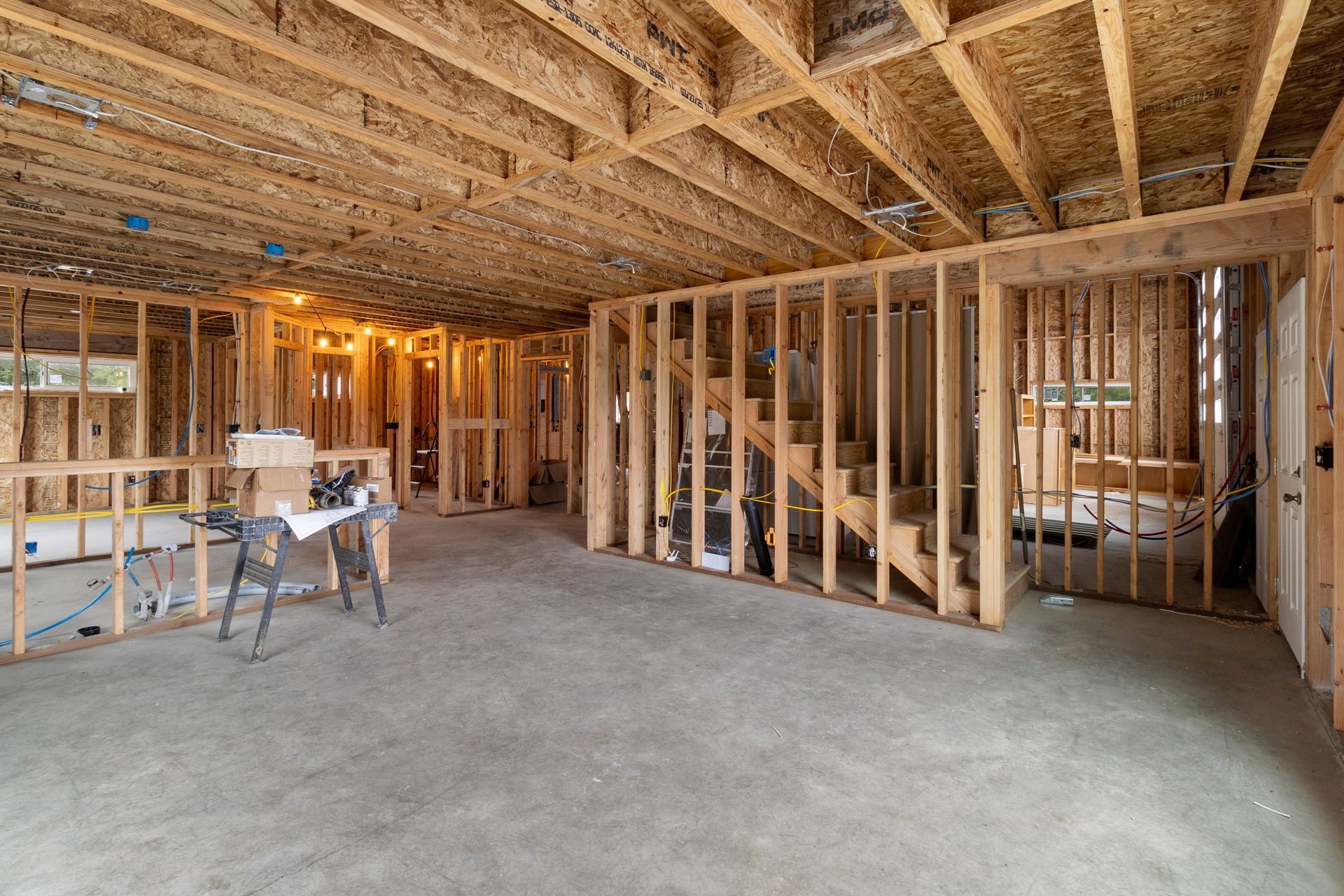 Interior view of a residential construction site featuring exposed wood framing, concrete flooring, and an open staircase.