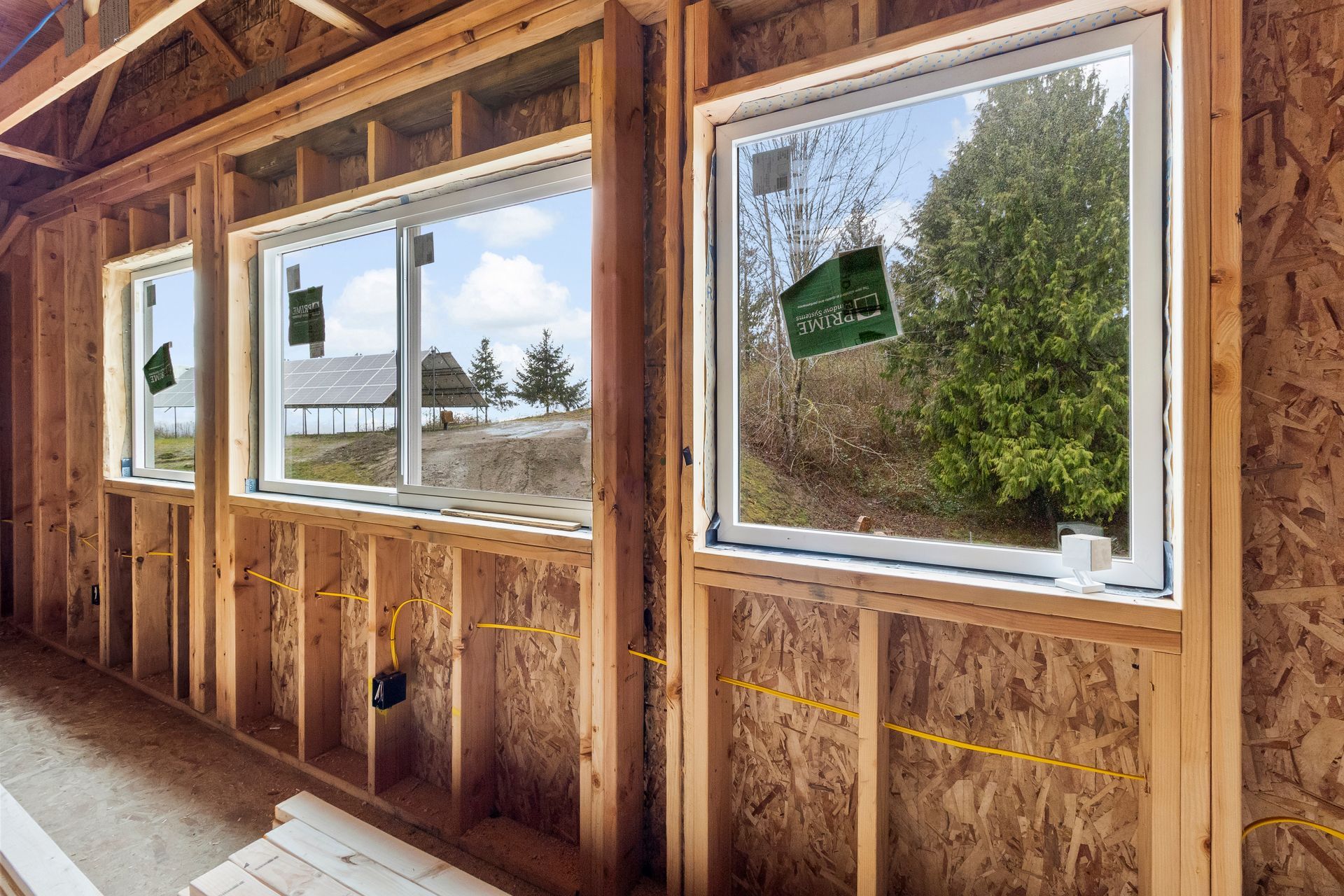 Unfinished interior wall frame with two installed windows overlooking a yard.