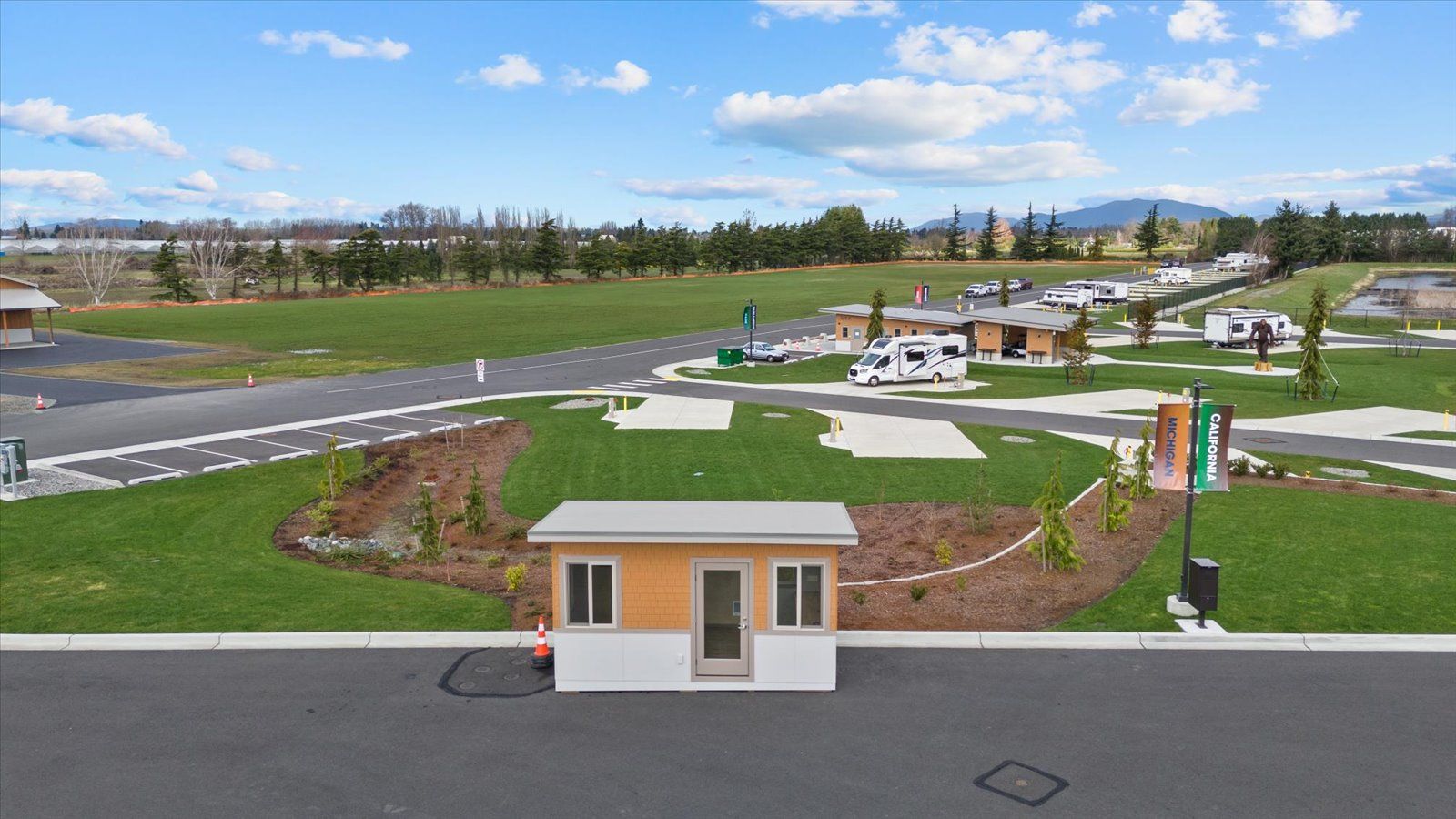 A small security kiosk sits in the foreground of a manicured RV park with several campers parked on green grass.
