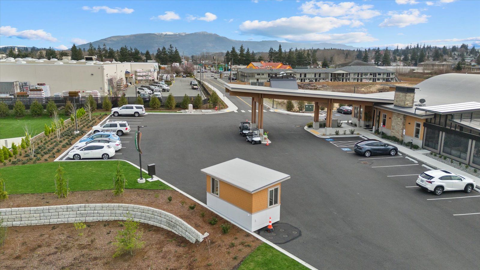 An elevated view of a paved parking lot with a small security kiosk, a covered entryway, and several parked vehicles.
