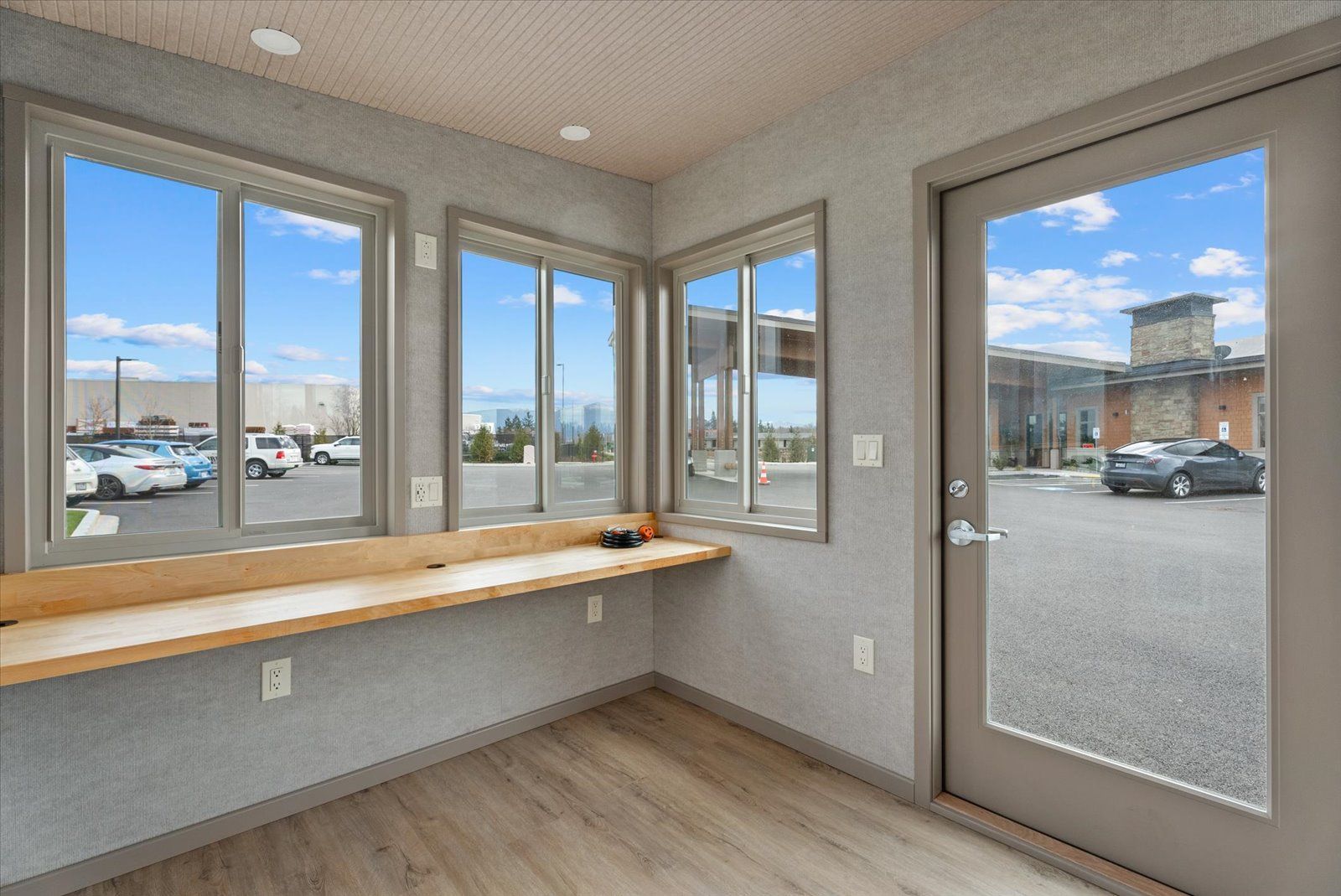 Interior view of a small security guard booth with windows, a wooden counter, and a glass door overlooking a parking lot.