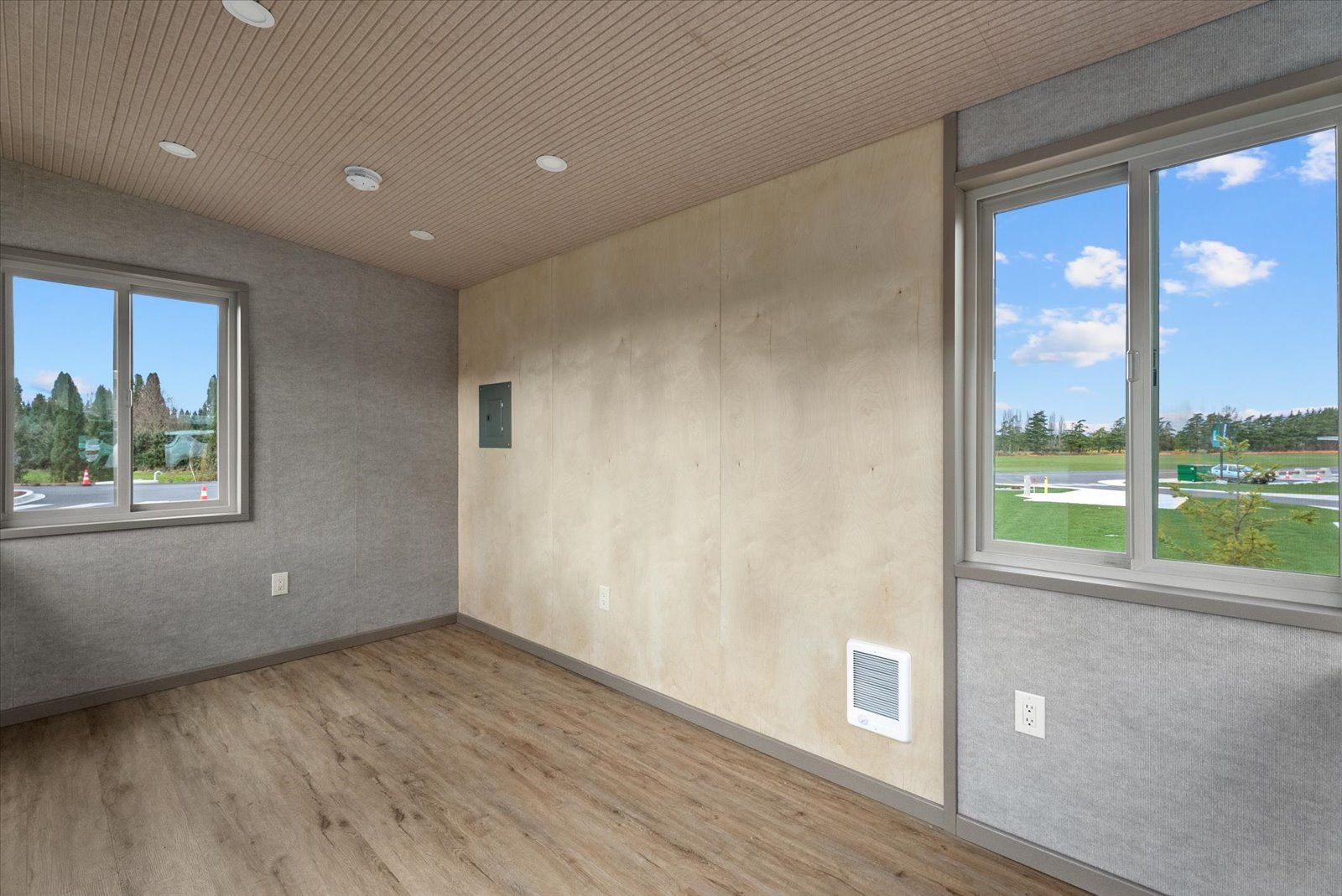 An empty room with wood-look flooring, a textured ceiling, grey walls, and a light-colored accent wall with two windows.