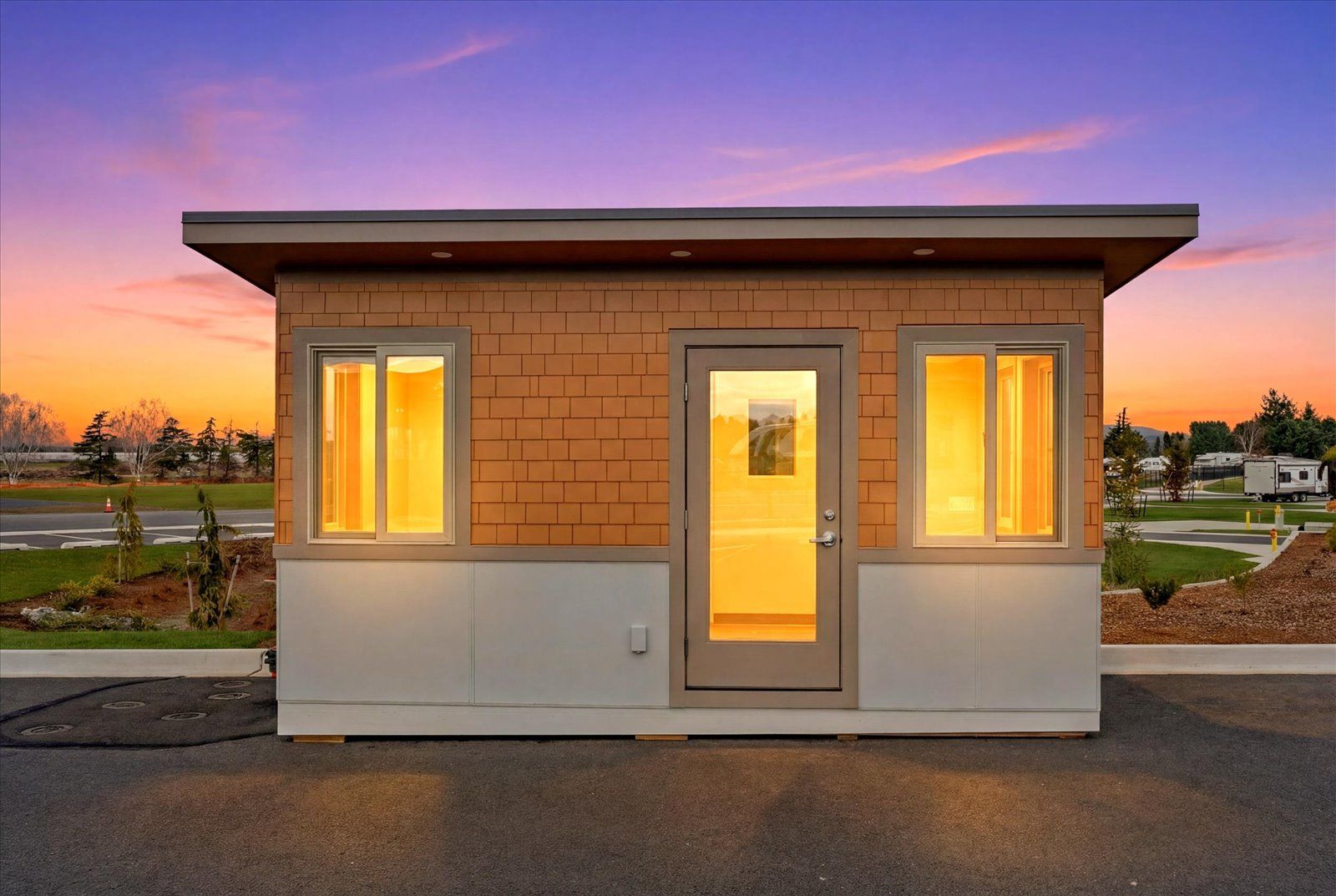 Small, modern structure with cedar shake siding, a centered door, and two side windows against a vibrant sunset sky.