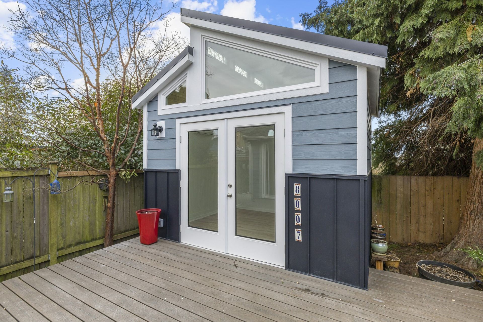 A blue and white shed with sliding glass doors is sitting on a wooden deck.