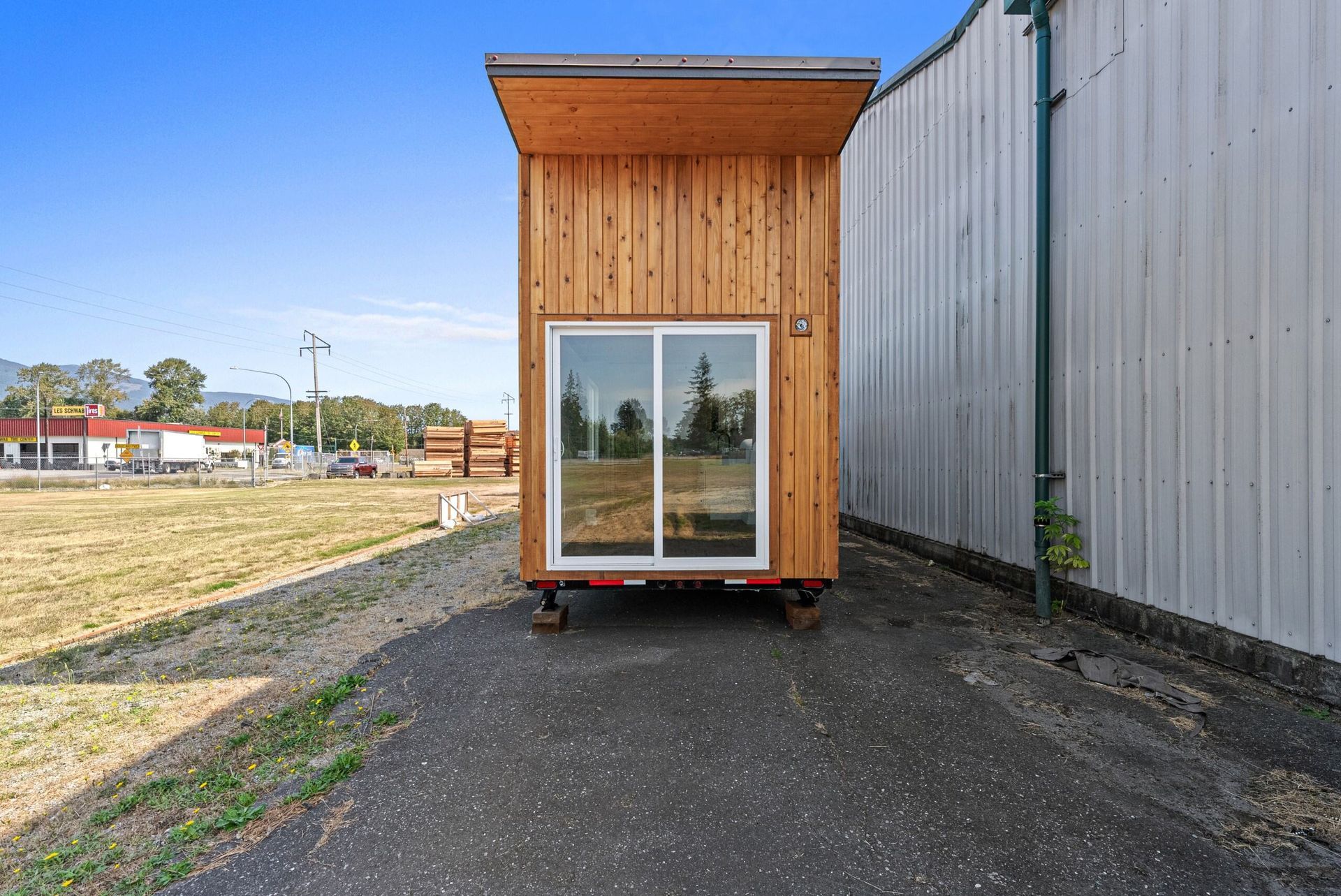 A small wooden house with a sliding glass door is parked next to a building.