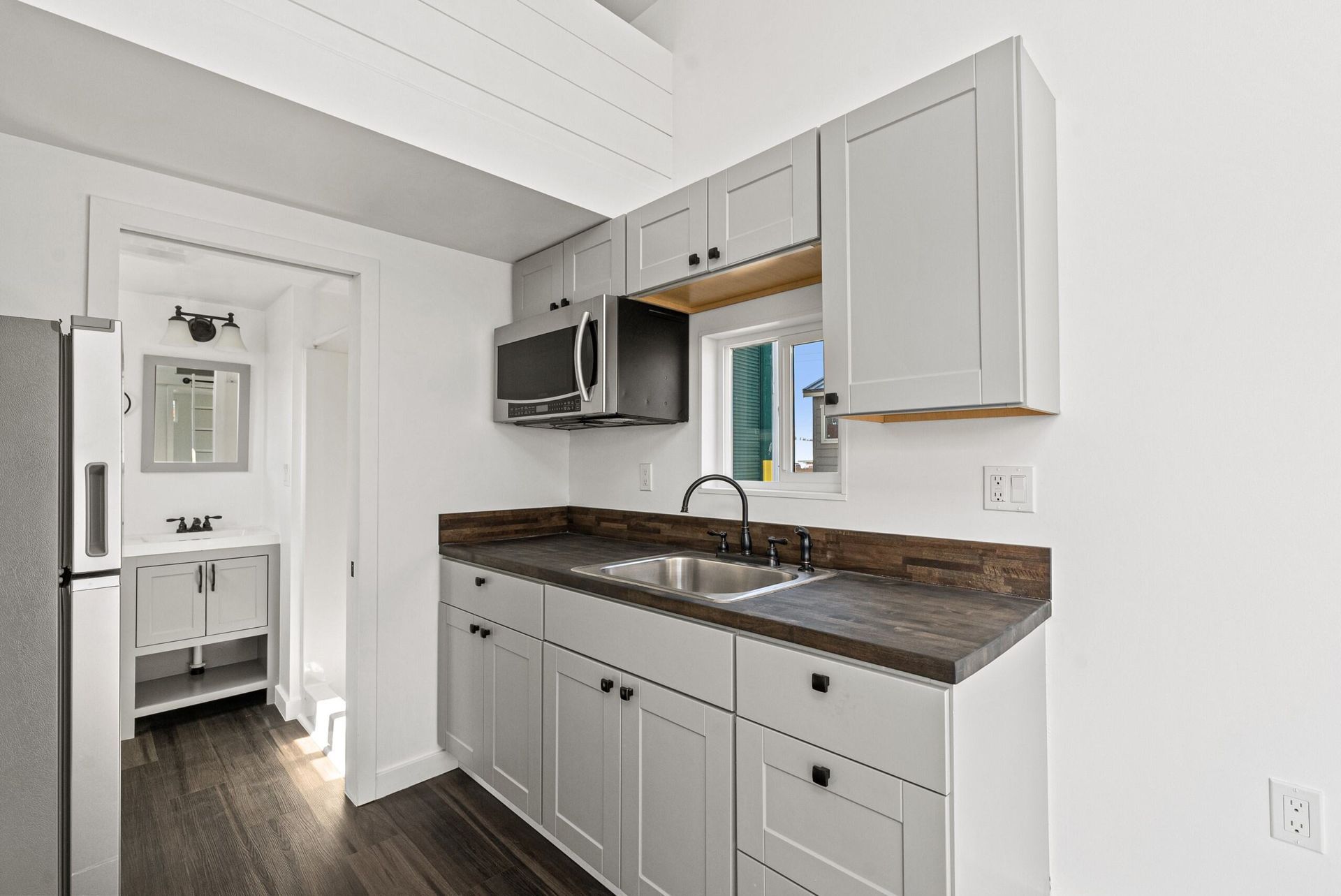 A kitchen with white cabinets, a sink, a refrigerator, and a microwave.