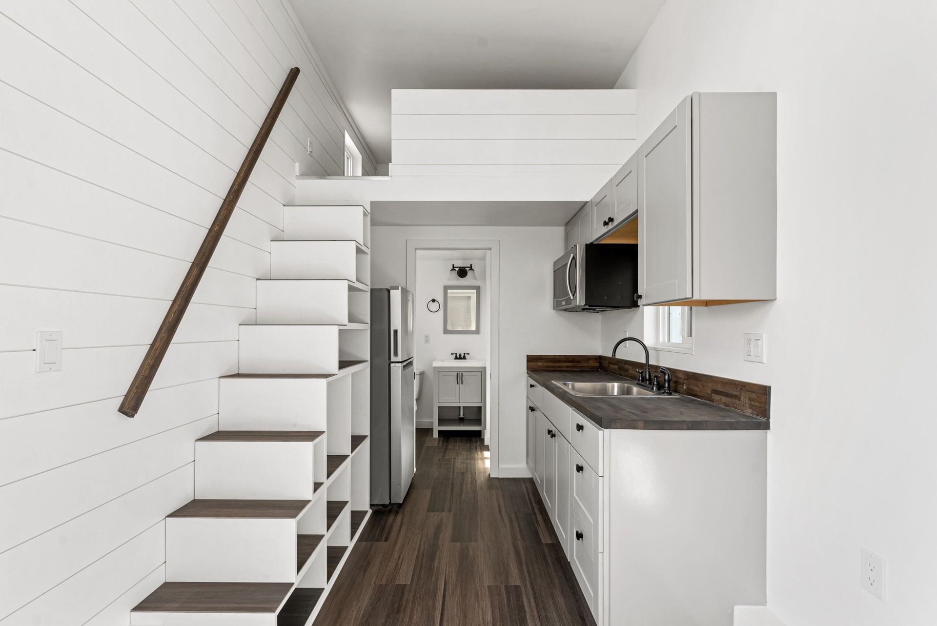 A small kitchen with stairs leading up to a loft.