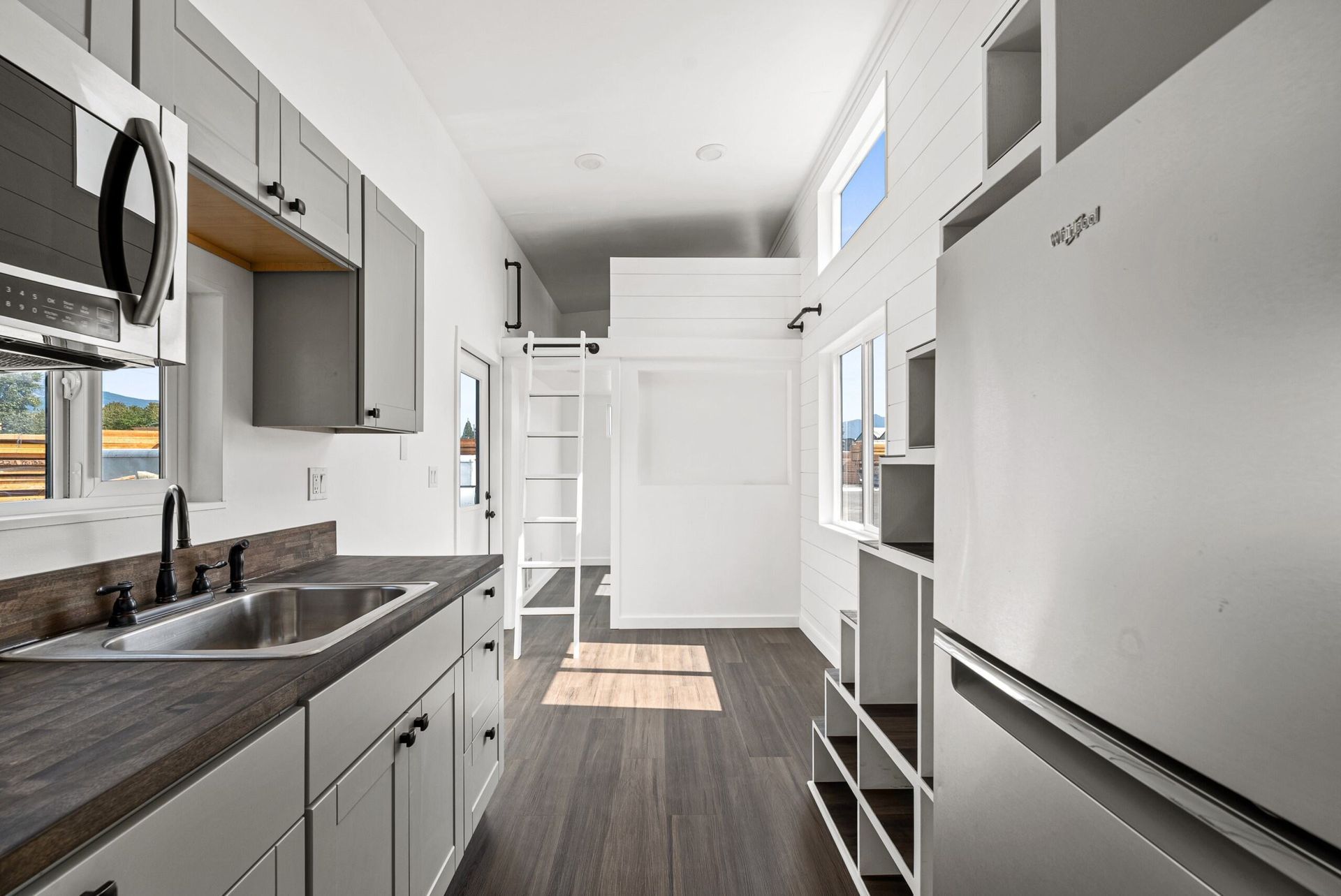 A kitchen with a sink, refrigerator, microwave, and ladder.