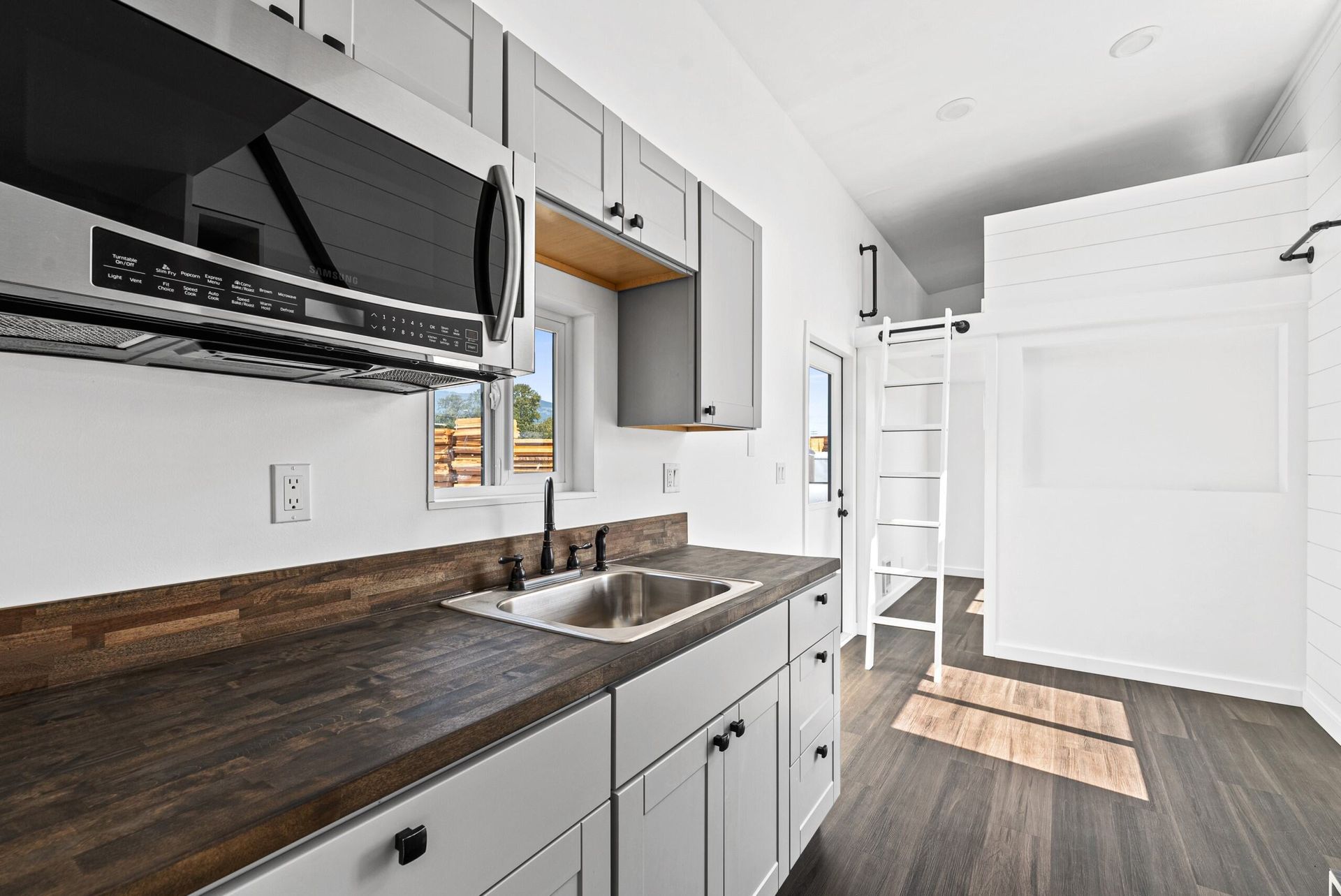 A kitchen with white cabinets, a sink, a microwave, and a window.