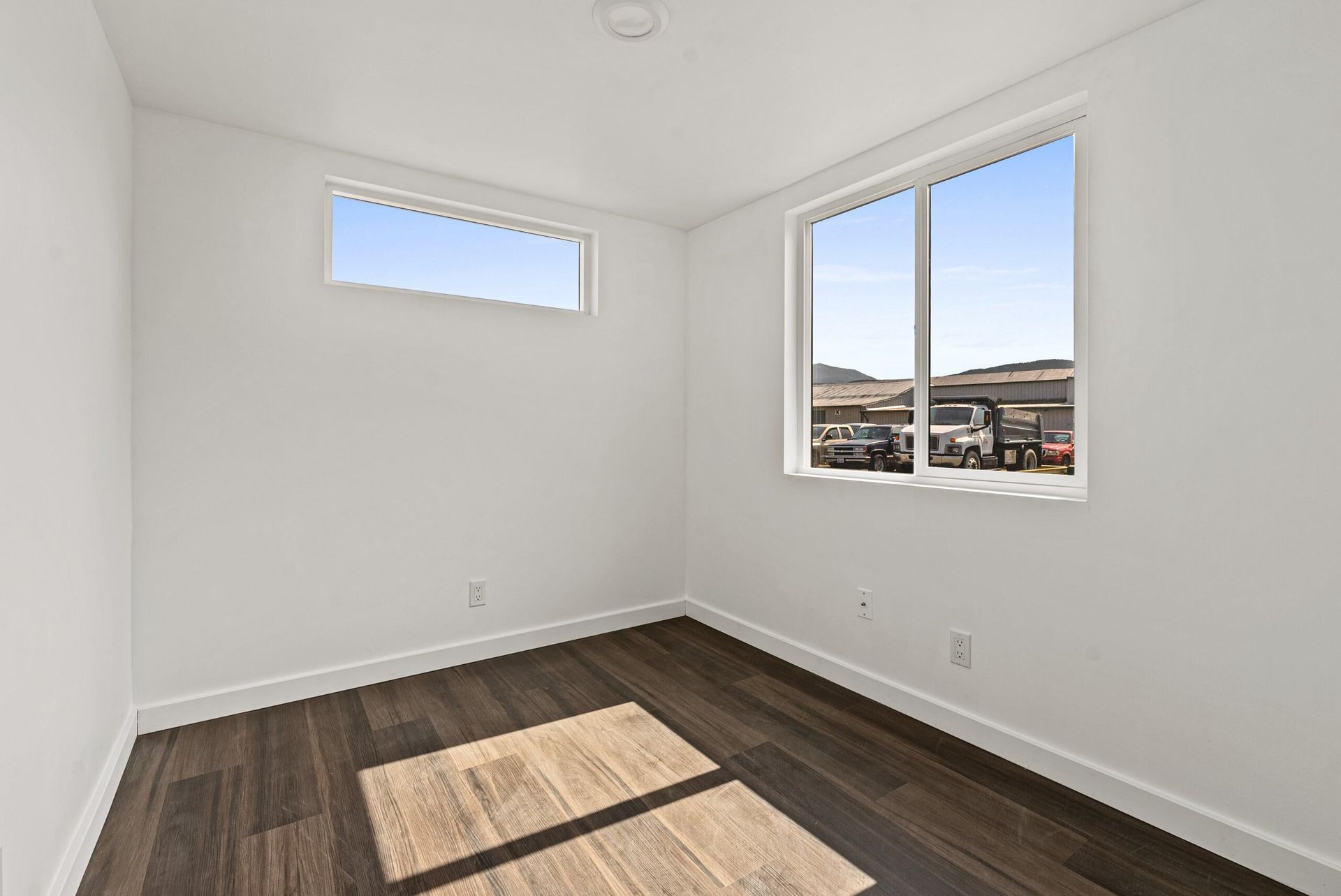 An empty room with hardwood floors and two windows.