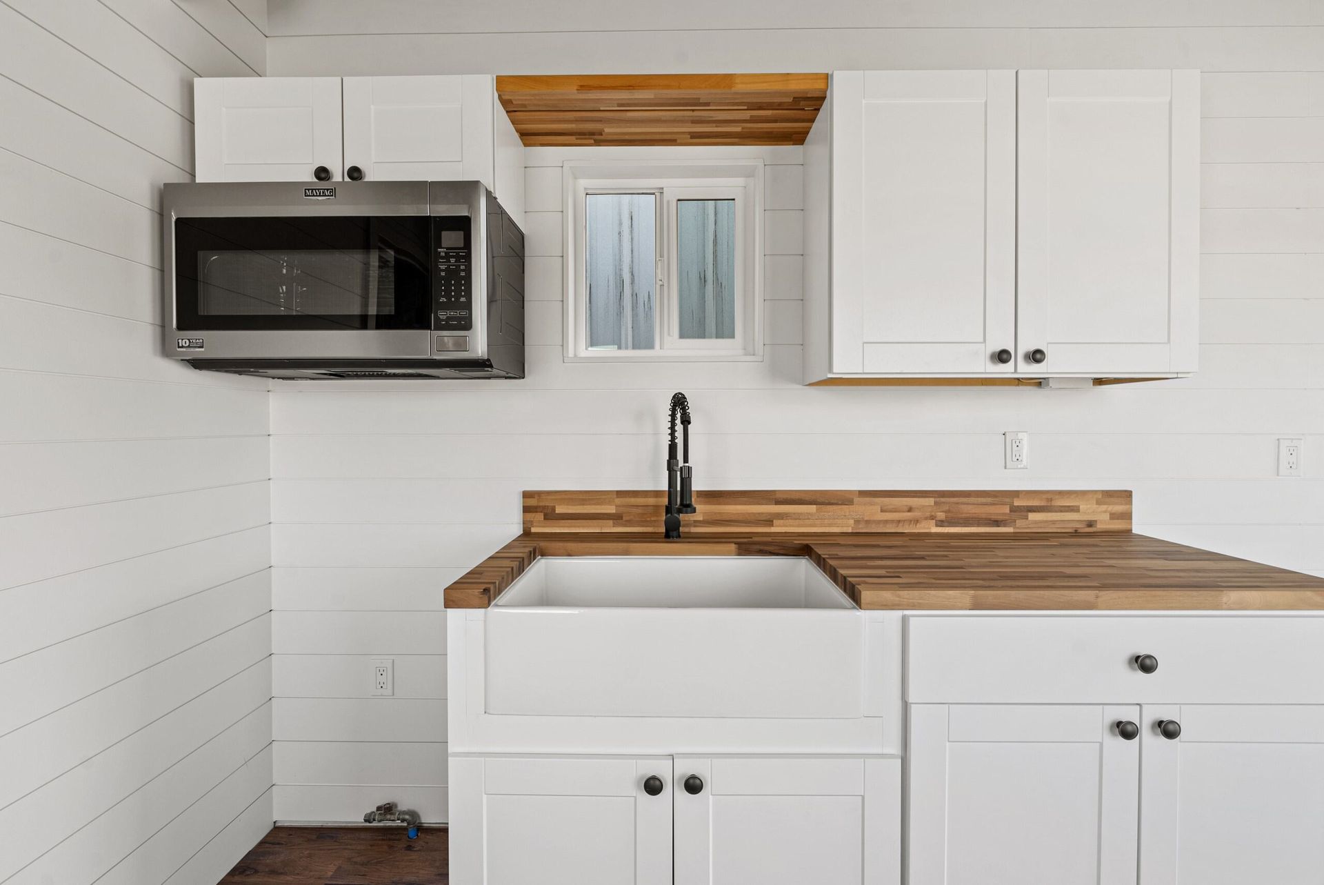 A kitchen with white cabinets, a sink, a microwave, and a window.