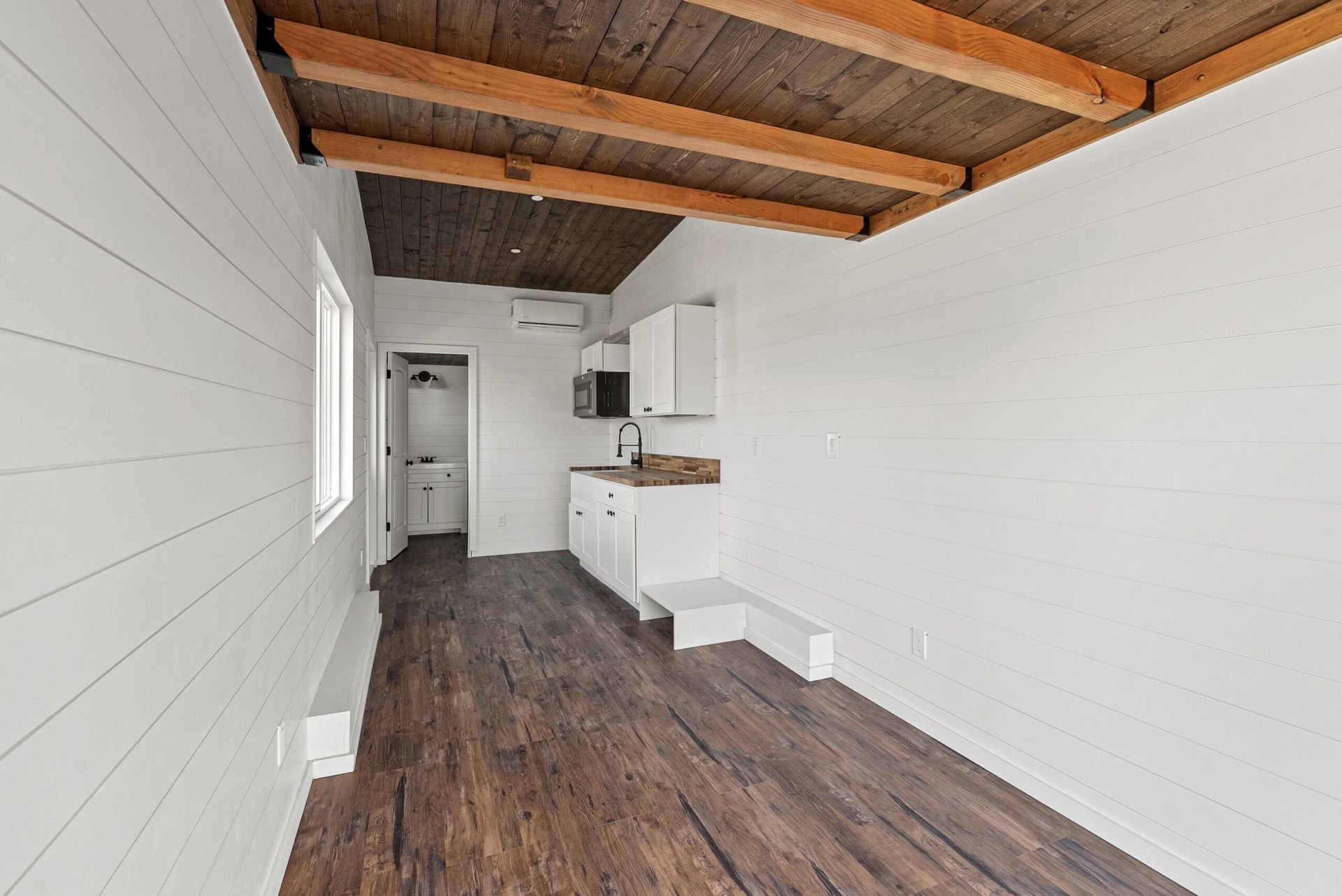 An empty room with white walls and wooden floors and a wooden ceiling.
