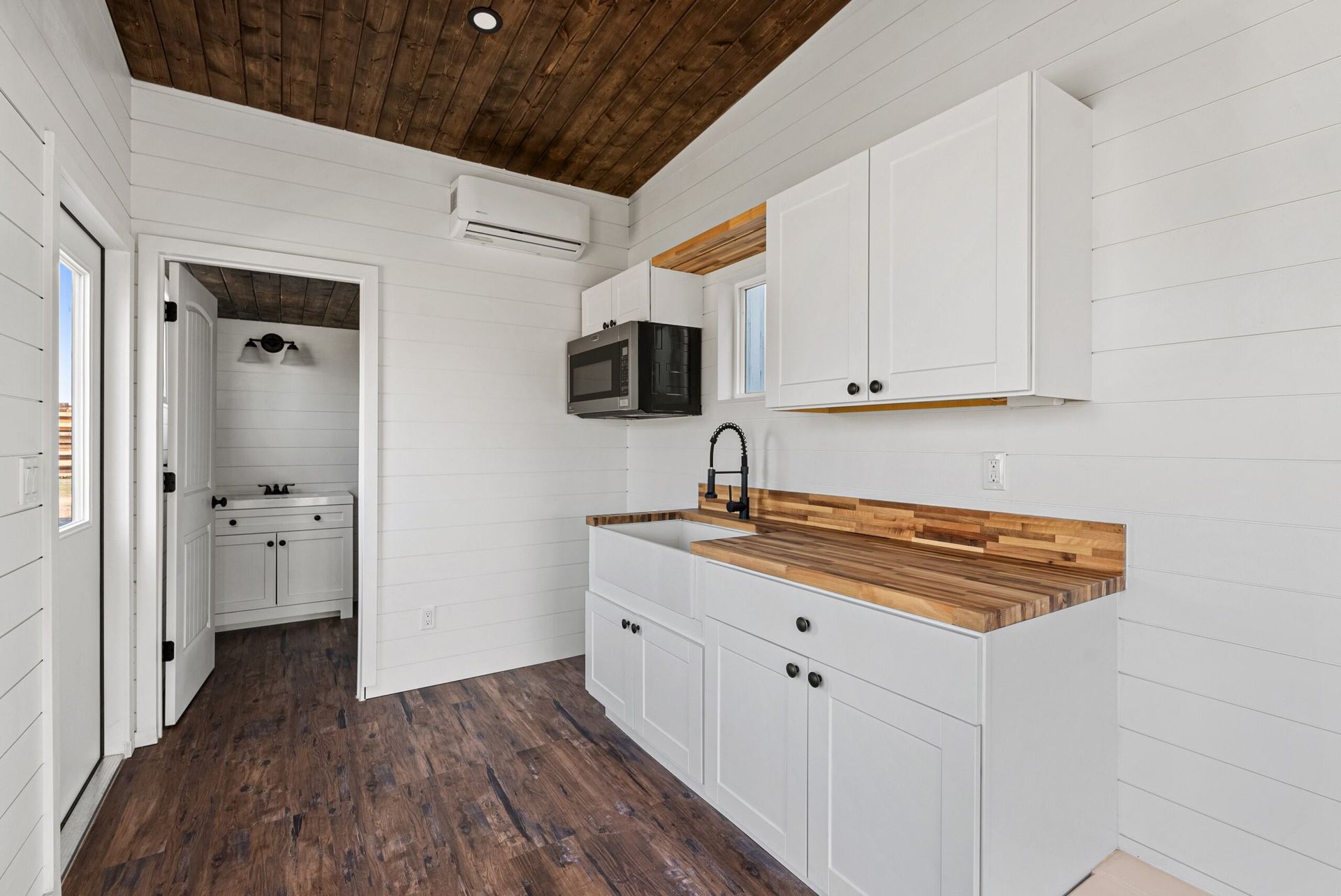 A kitchen with white cabinets, wooden counter tops, and a microwave.