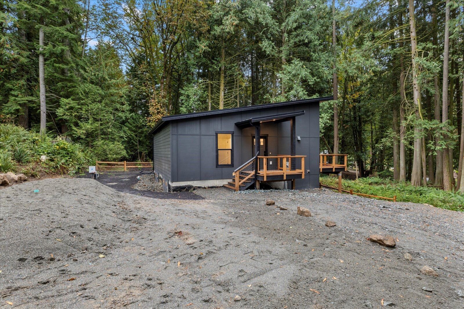 A small black house with a porch in the middle of a forest.
