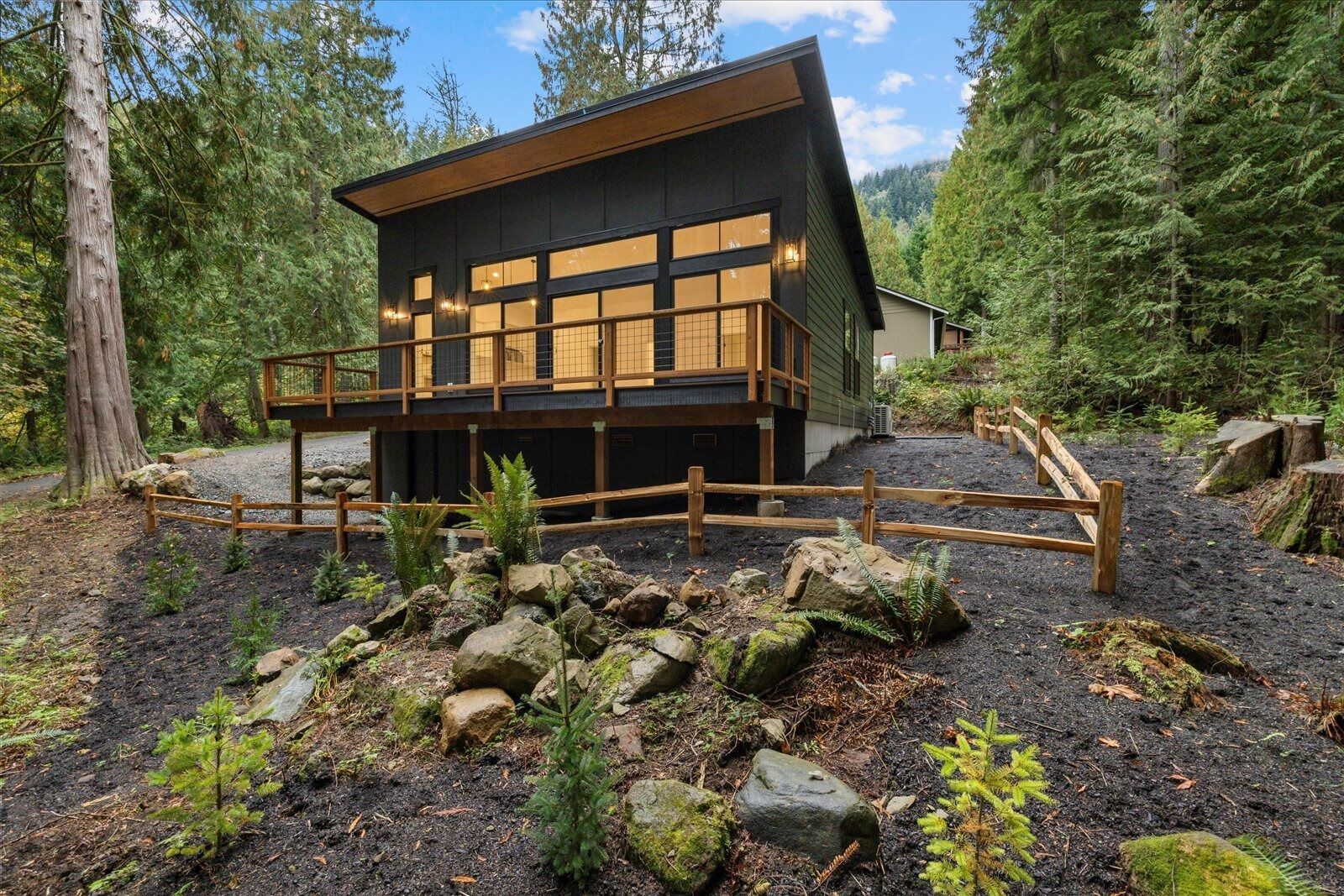 A small house in the middle of a forest with a wooden fence around it.