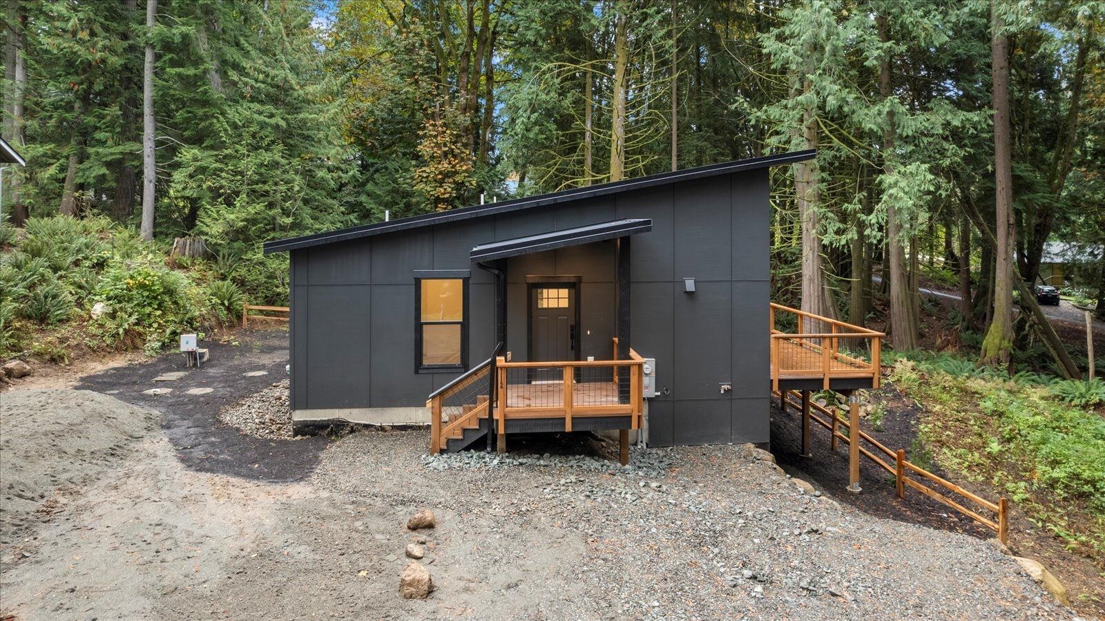 A small black house with a wooden deck in the middle of a forest.
