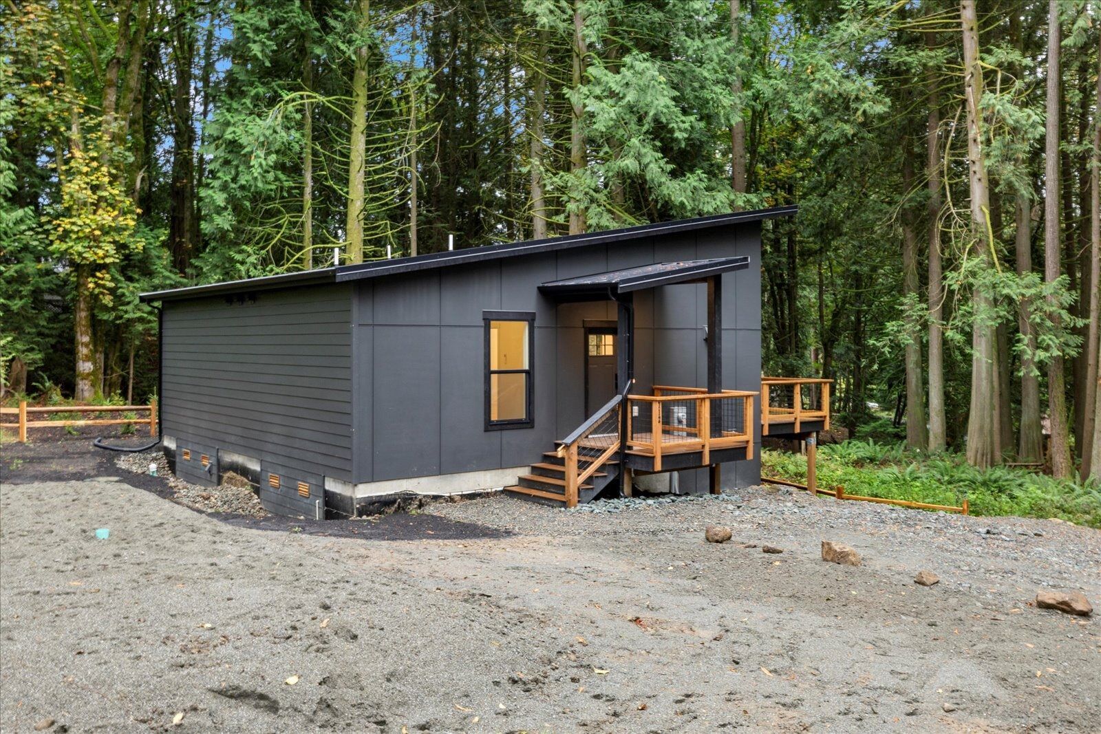 A small black house with a porch in the middle of a forest.