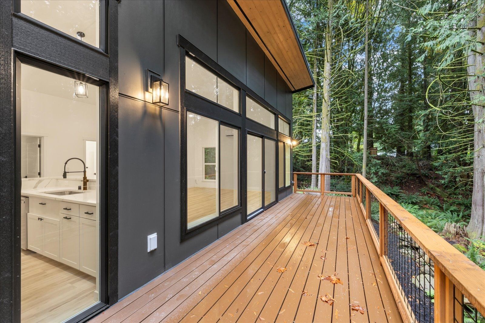 A large wooden deck with a railing in front of a house surrounded by trees.
