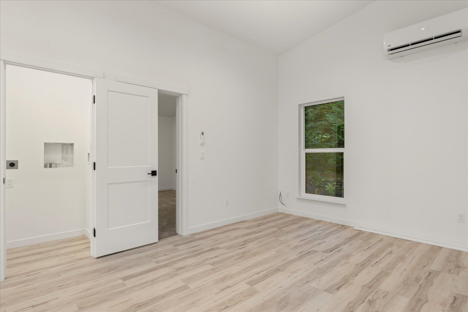 An empty room with hardwood floors, white walls and a window.
