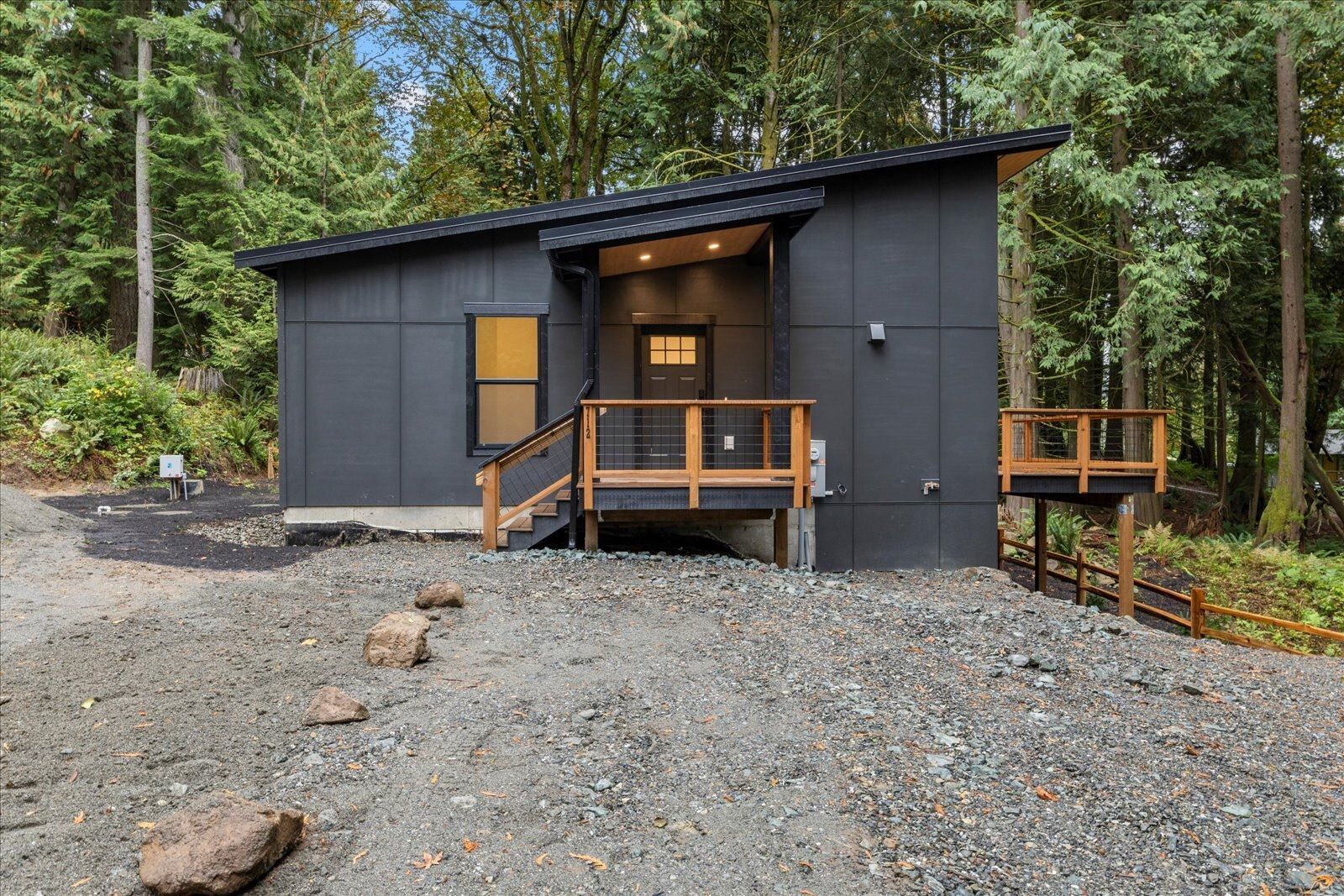 A small black house with a wooden deck in the middle of a forest.
