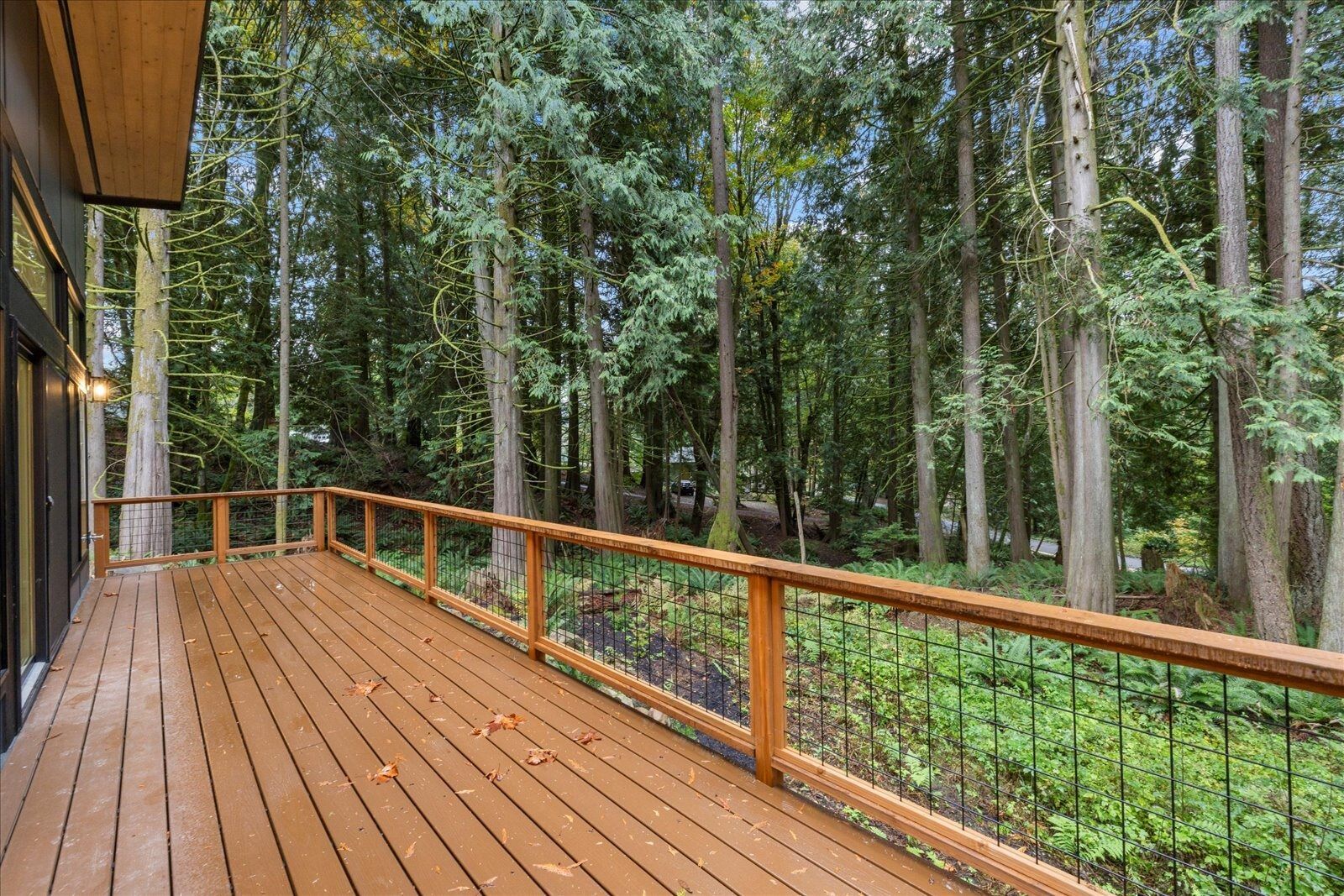 A wooden deck with a metal railing overlooking a forest.