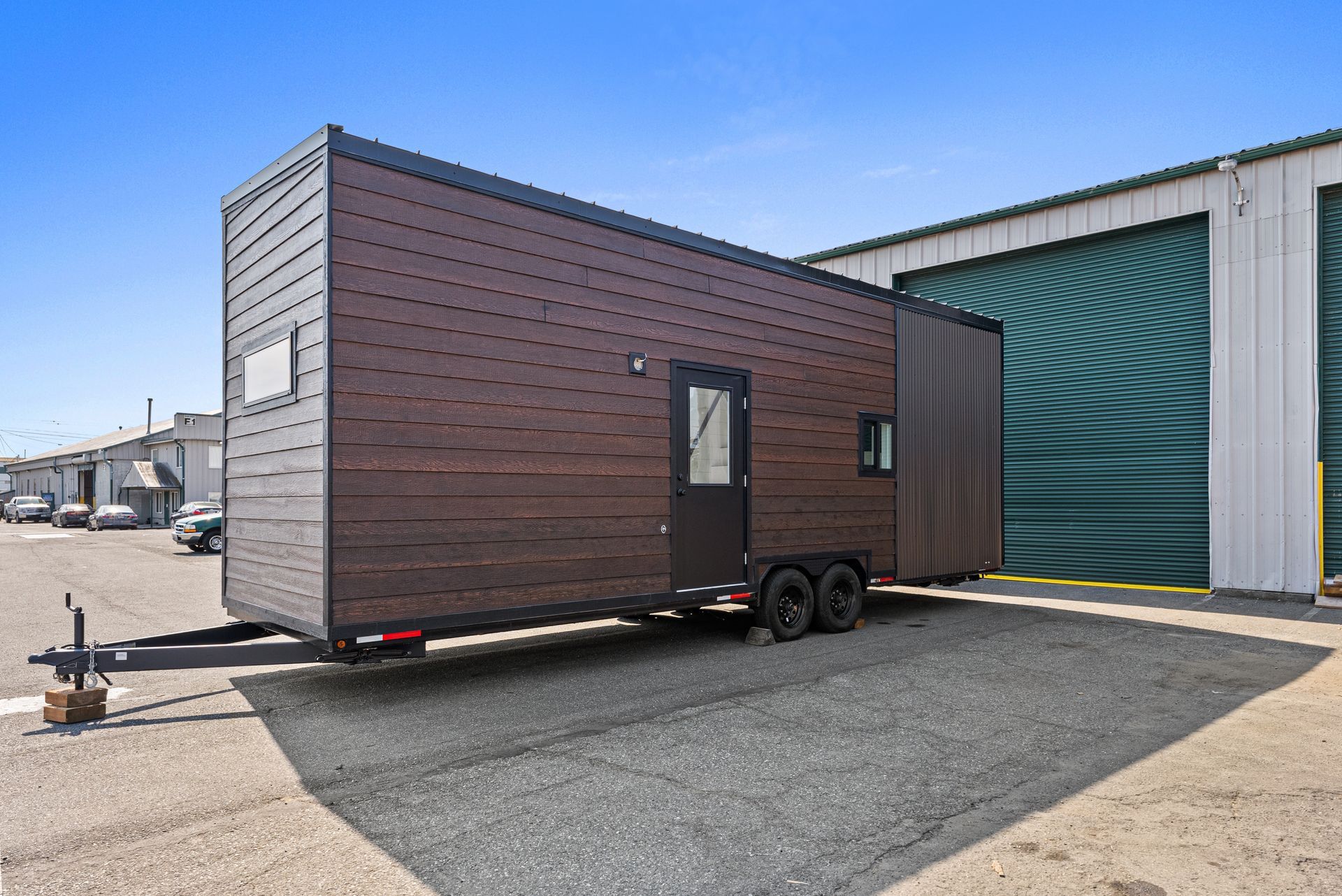 A tiny house on a trailer is parked in front of a building.