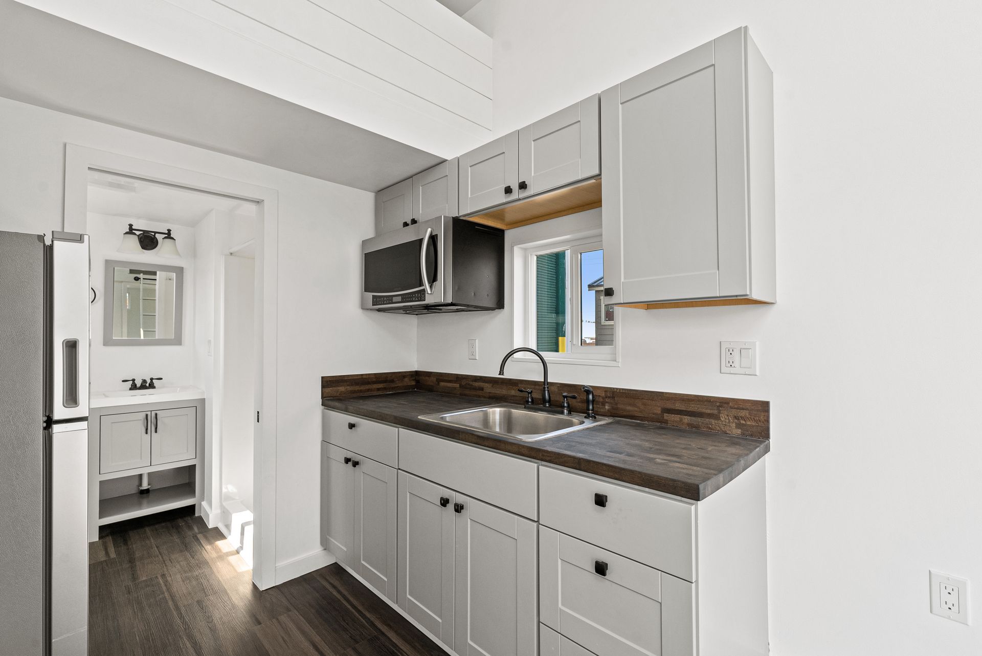 A kitchen with white cabinets, a sink, a refrigerator, and a microwave.