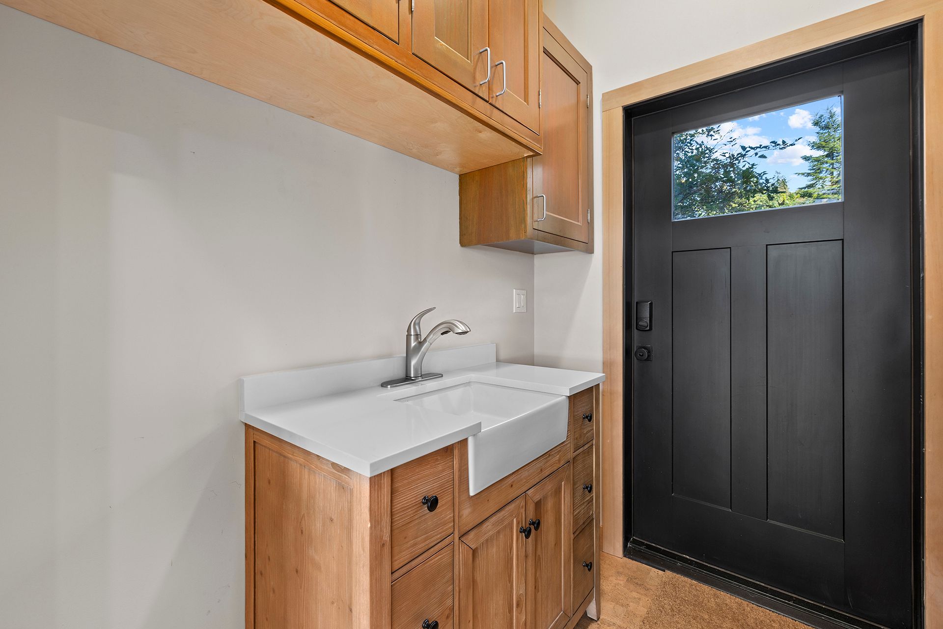 A laundry room with a sink, cabinets, and a black door.