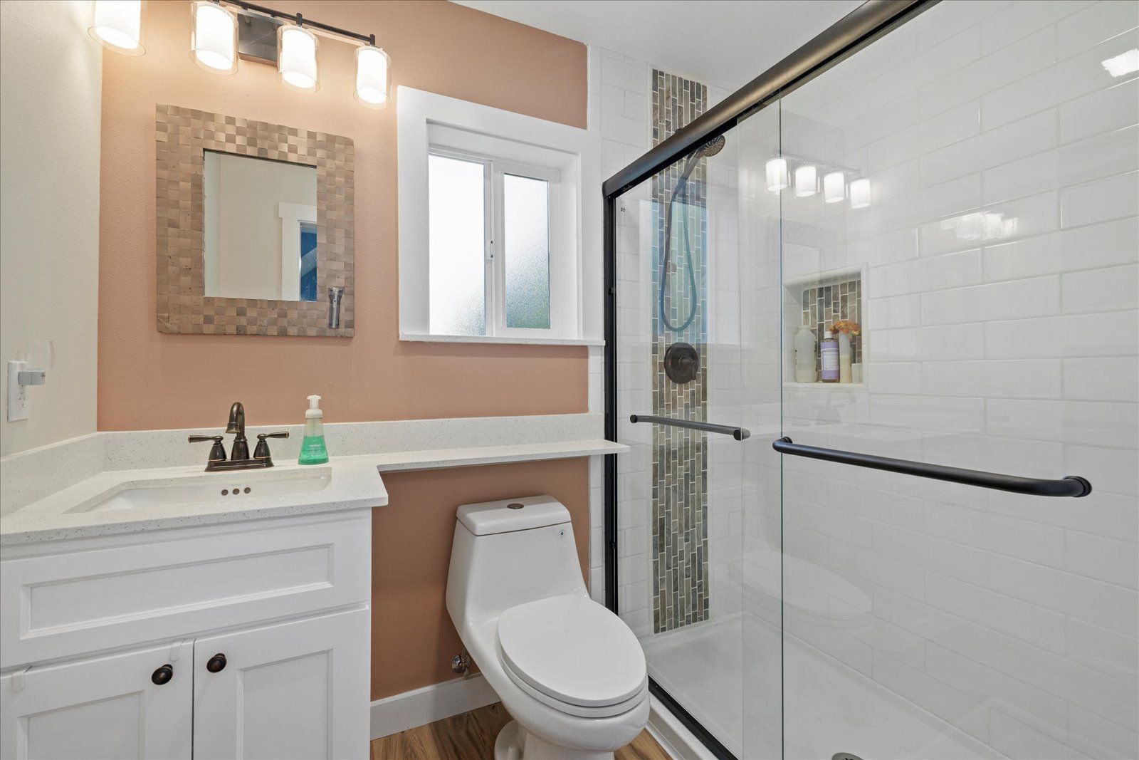 A bathroom with a toilet, sink, mirror, and walk-in shower.
