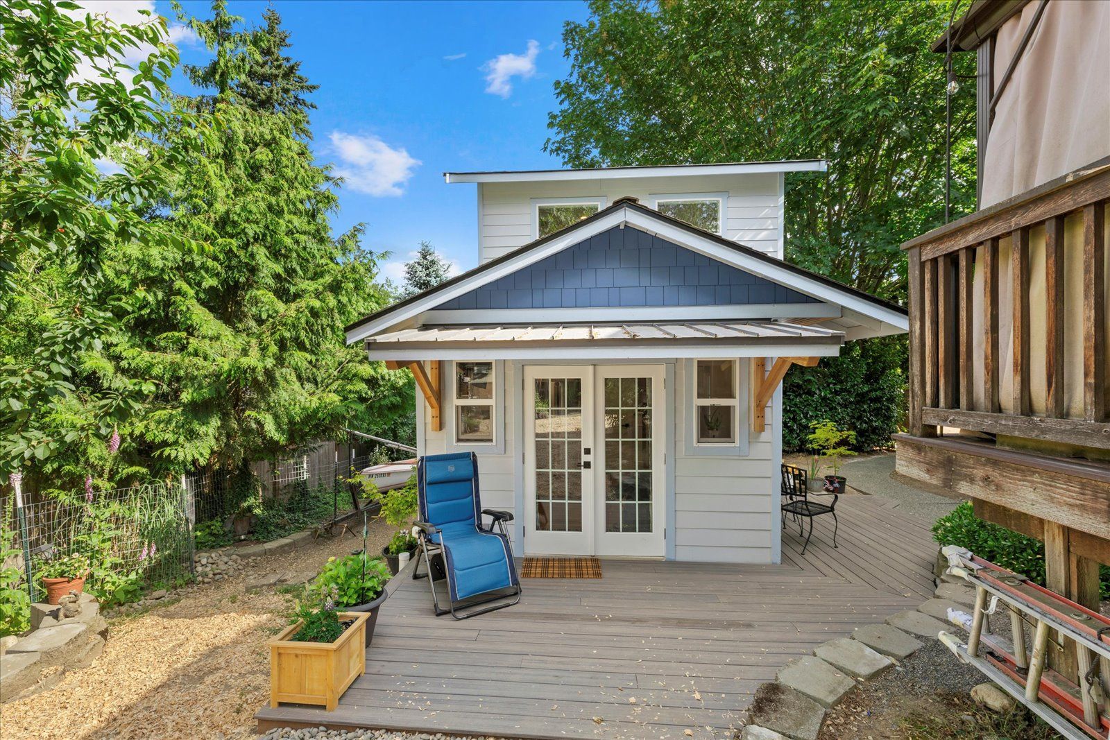 A small white house with a blue roof and a blue chair on the deck.